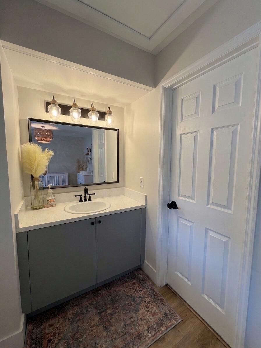 Vanity featuring a solid-surface countertop with an integrated oval sink, matte black hardware, four-light wall fixture, and framed mirror