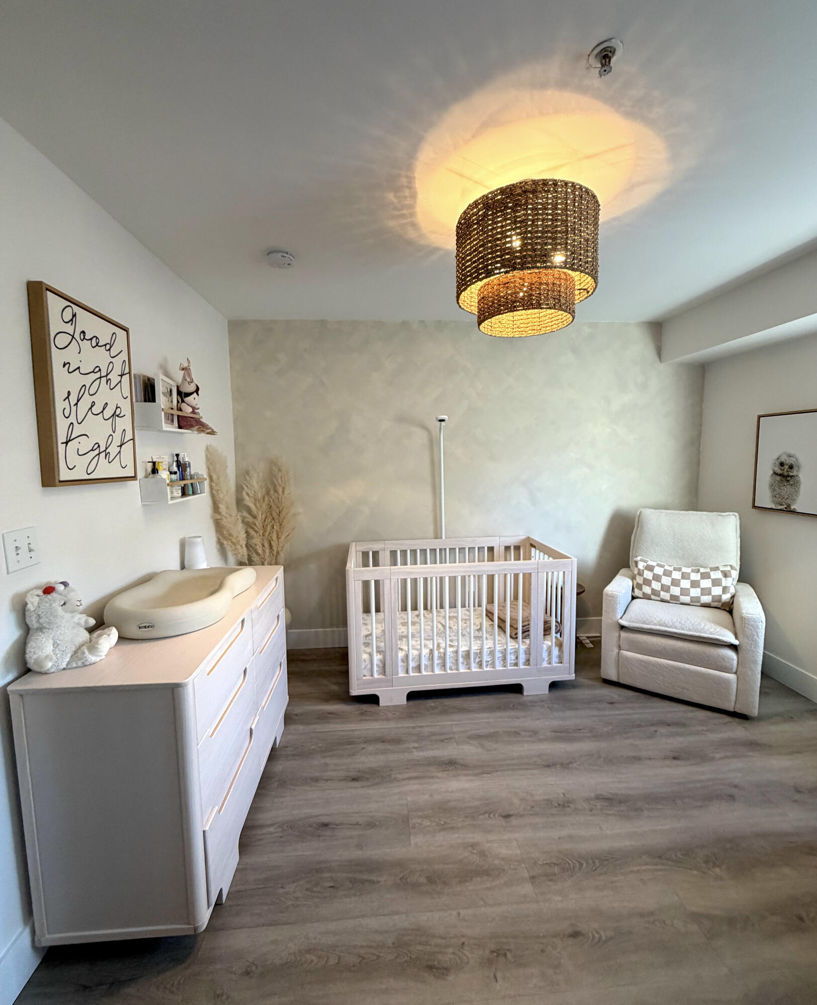 Bedroom featuring wood-finish flooring, a textured accent wall, and a multi-tiered woven drum light fixture