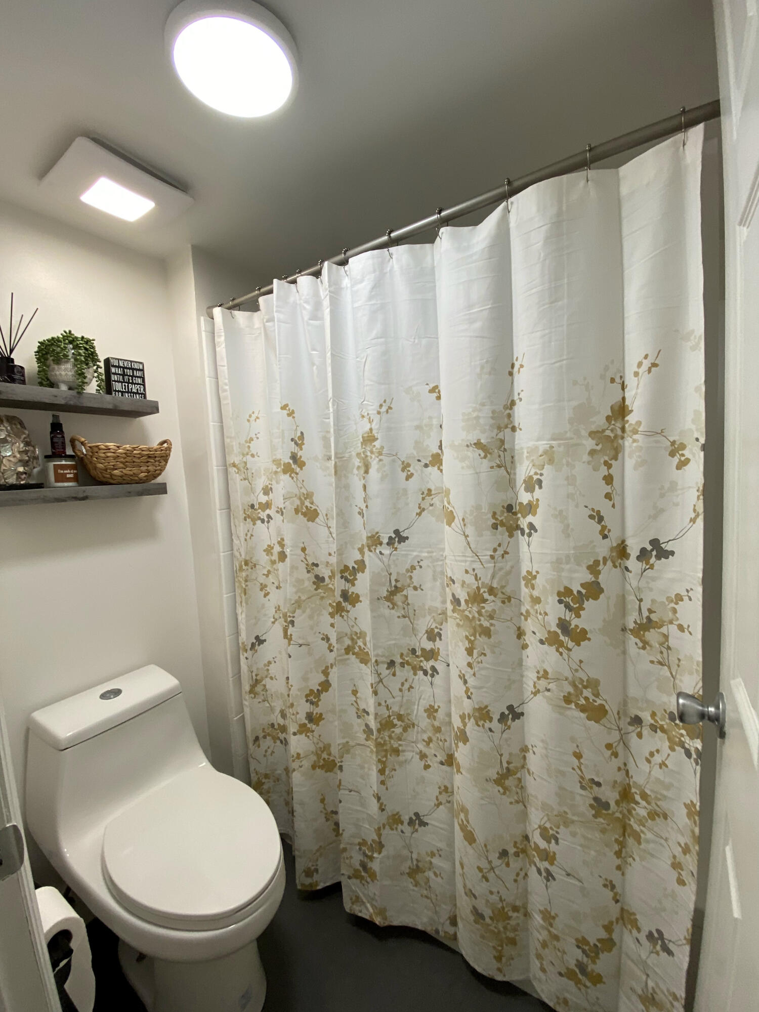 Full bathroom featuring a high-efficiency dual-flush toilet, recessed ceiling lighting, a shower enclosure with a stainless steel tension rod, and dual wall-mounted floating shelves