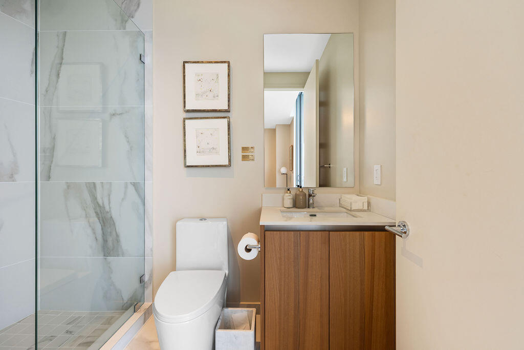 Bathroom featuring a glass-enclosed shower with large-format tile surround, a wood-finish vanity with a stone-surface countertop, an integrated sink, and a wall-mounted mirror