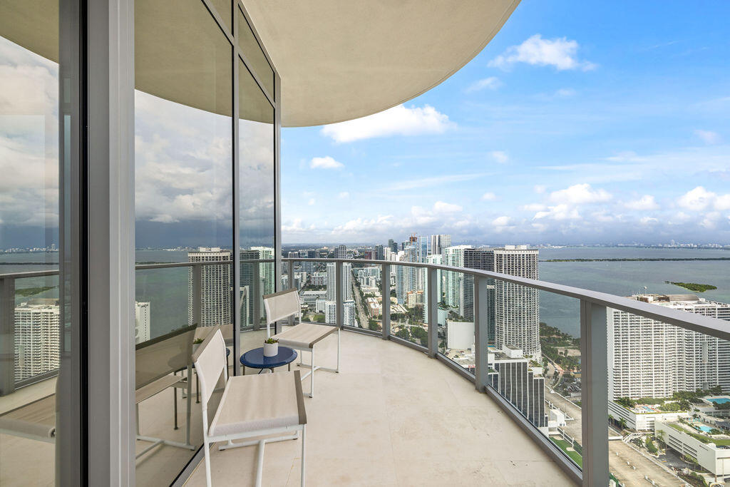 Curved private balcony featuring floor-to-ceiling glass wall, light-toned stone tile flooring, and a metal railing
