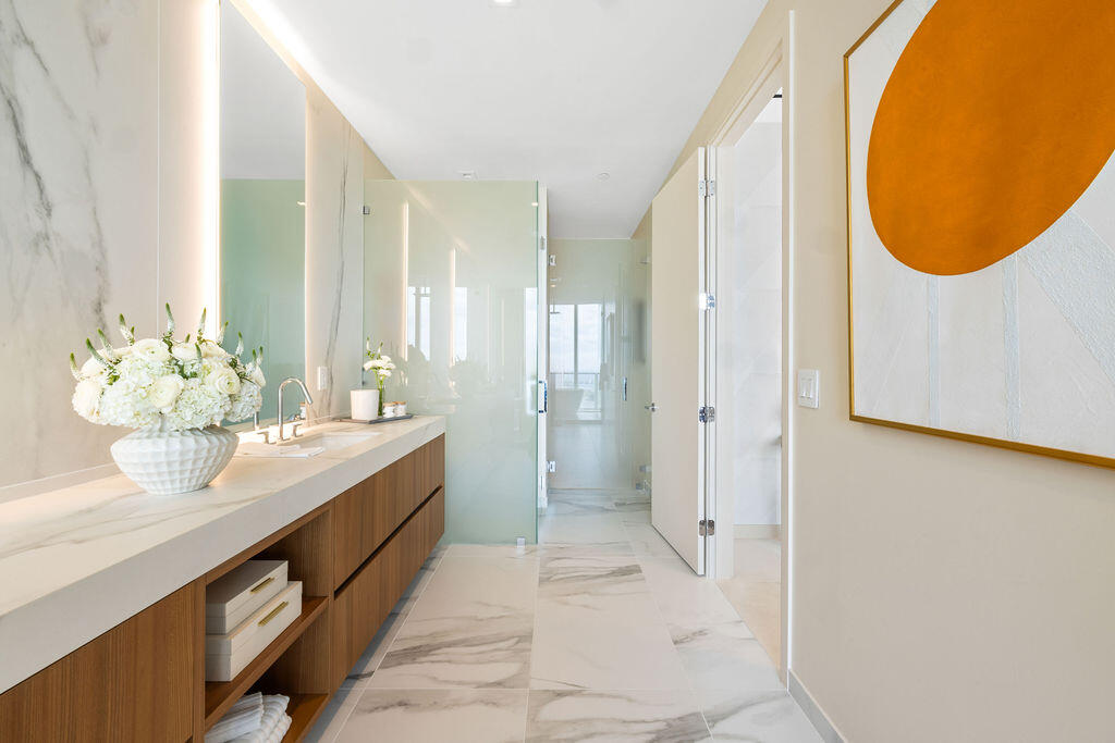Floating wood-finish vanity with countertop, integrated wall-to-ceiling mirror, stone-finish tile flooring, and glass-enclosed shower
