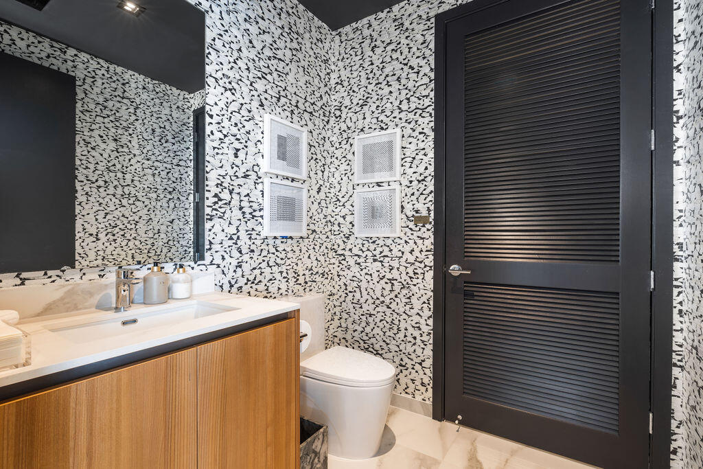 Floating wood-finish vanity with an integrated sink, large-scale wall mirror, patterned wall treatment, and black louvered door