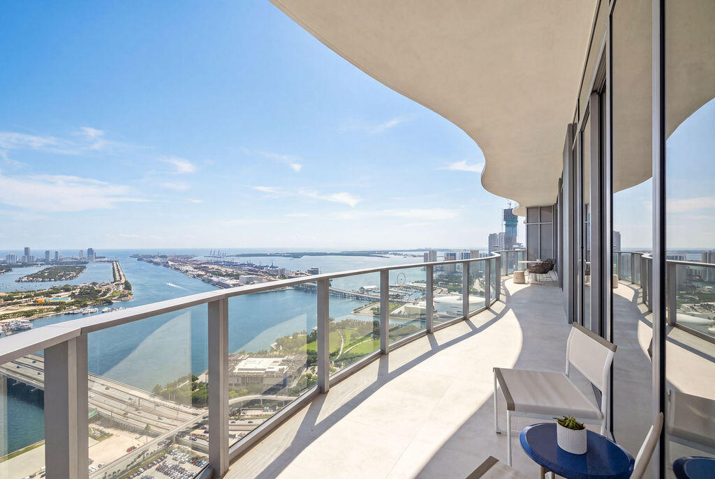 Curved balcony featuring a glass railing system, concrete flooring, and an overhanging structural soffit