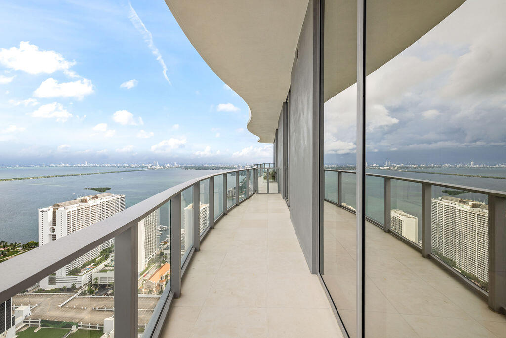 Curved balcony featuring light-colored tile flooring, a glass panel railing, and full-height floor-to-ceiling windows