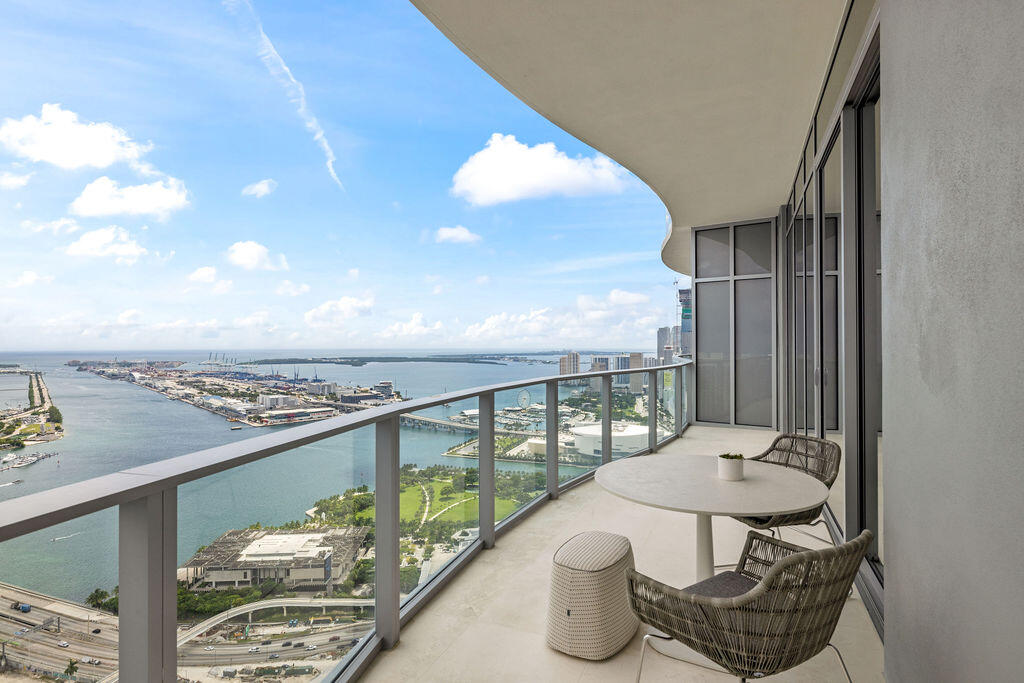 Covered wrap-around balcony featuring glass panel railings, neutral stone-finish flooring, and floor-to-ceiling glass windows