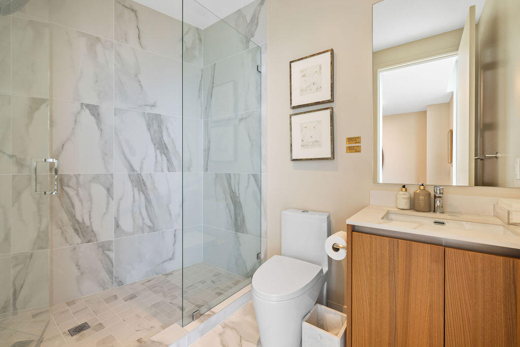 Walk-in shower with floor-to-ceiling stone-finish wall tiles and a glass enclosure, wood-finish vanity with an integrated countertop sink, and a large wall-mounted mirror