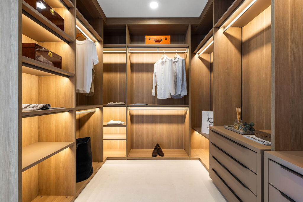 Custom closet featuring light wood-finish cabinetry, integrated LED shelf lighting, tiered hanging rods, and built-in dresser drawers with matte hardware