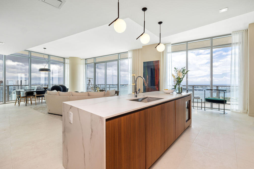 Kitchen island featuring a waterfall stone countertop, wood-finish cabinetry, an undermount sink, and polished metal faucet
