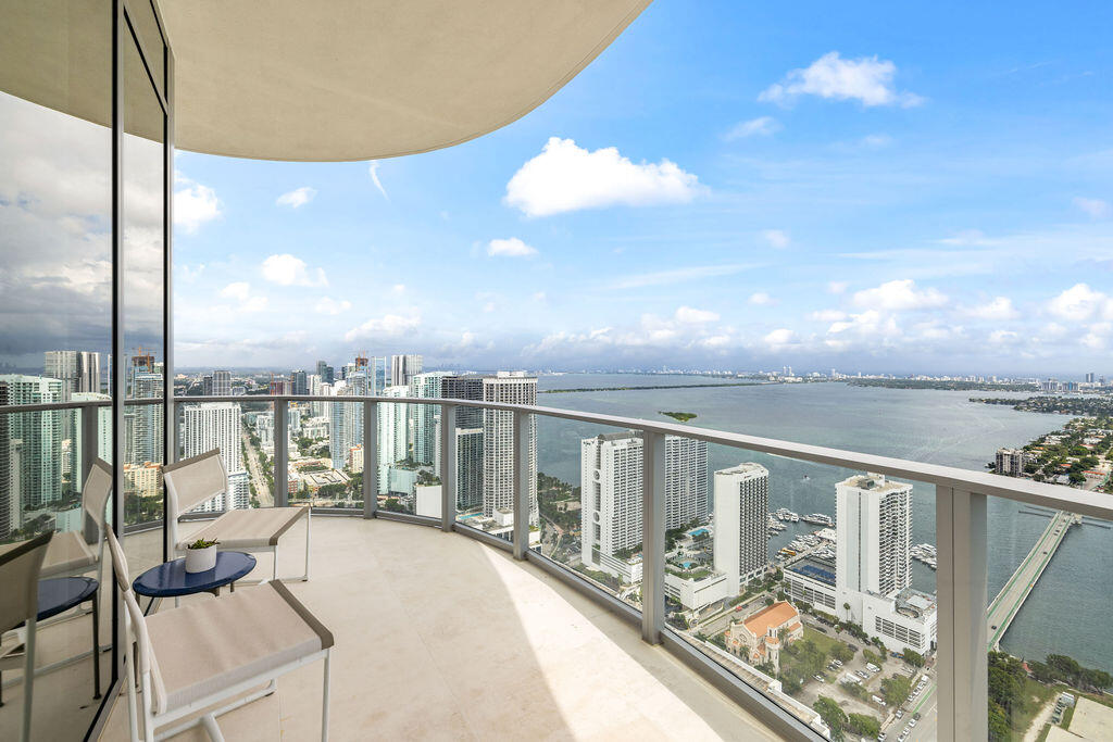 Curved balcony featuring light-colored stone flooring, a glass railing, and panoramic water and city skyline outlooks