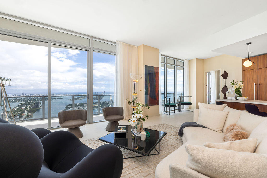 Floor-to-ceiling glass windows, expansive private balcony with glass railing, open-concept living area, custom flat-panel wood cabinetry, and neutral tile flooring