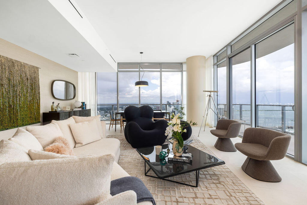 Floor-to-ceiling glass walls, sleek cylindrical architectural column, recessed linear lighting, polished neutral flooring, and integrated balcony access