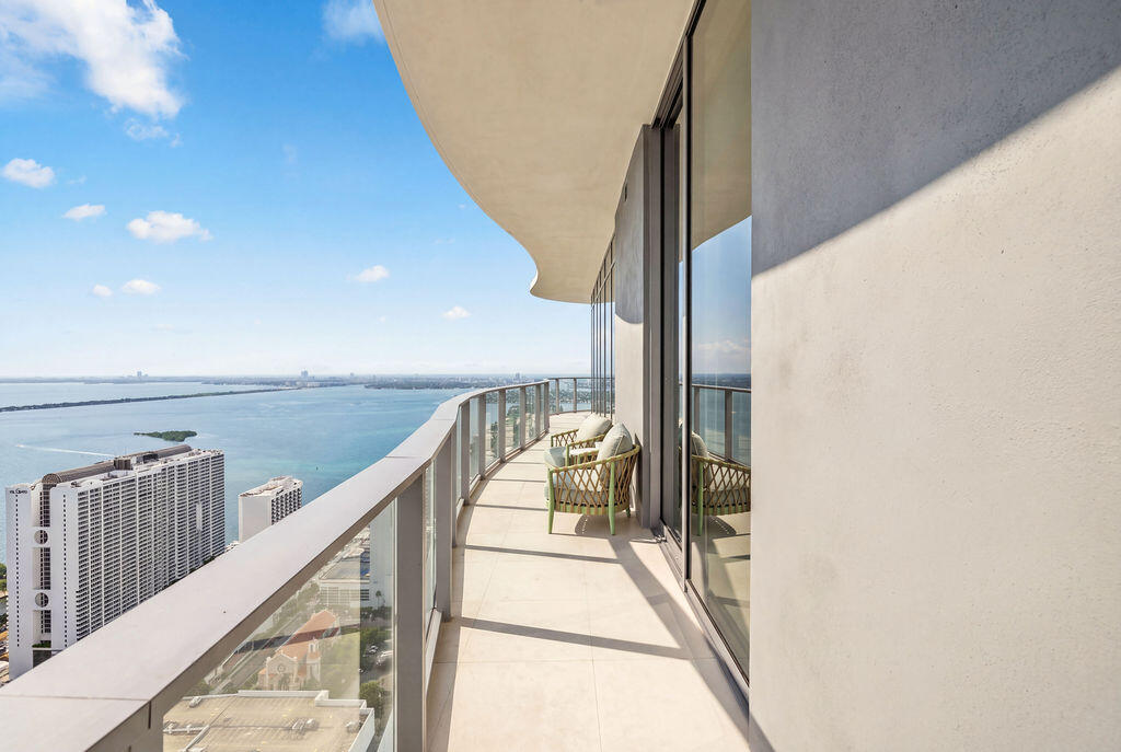 Curved exterior balcony featuring tile flooring, a glass-panel railing, and floor-to-ceiling glass sliding doors