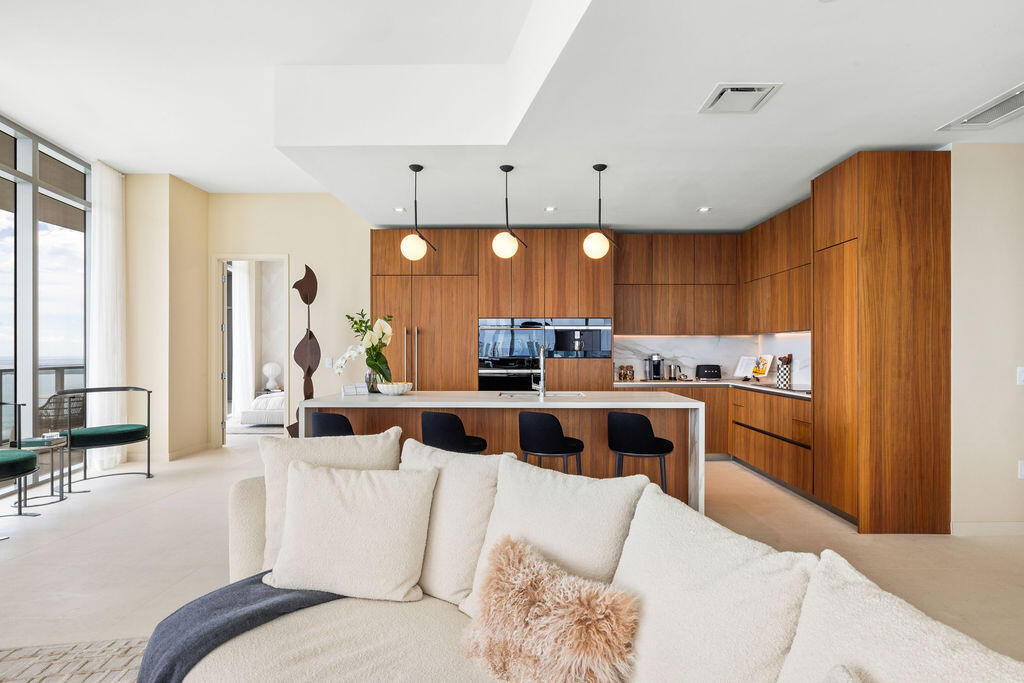 Modern kitchen featuring flat-panel wood cabinetry, a waterfall-edge kitchen island, stone backsplash, built-in wall oven, and three globe pendant lights
