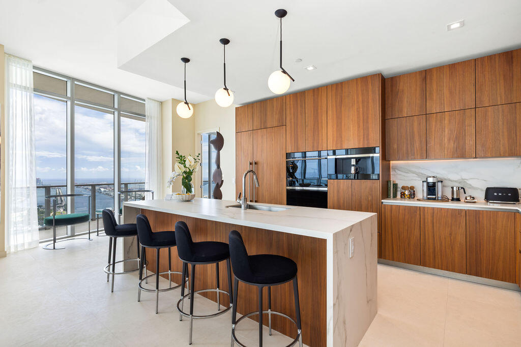 Kitchen featuring flat-panel wood cabinetry, stone-finish waterfall island with an undermount sink, built-in stainless steel appliances, and spherical pendant lighting