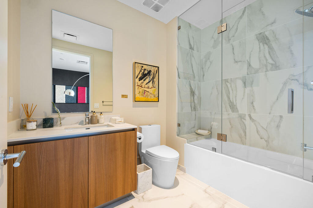 Bathroom featuring a wood-finish vanity with a light-toned countertop, a frameless glass shower enclosure, large-format tile shower surround, and tile flooring