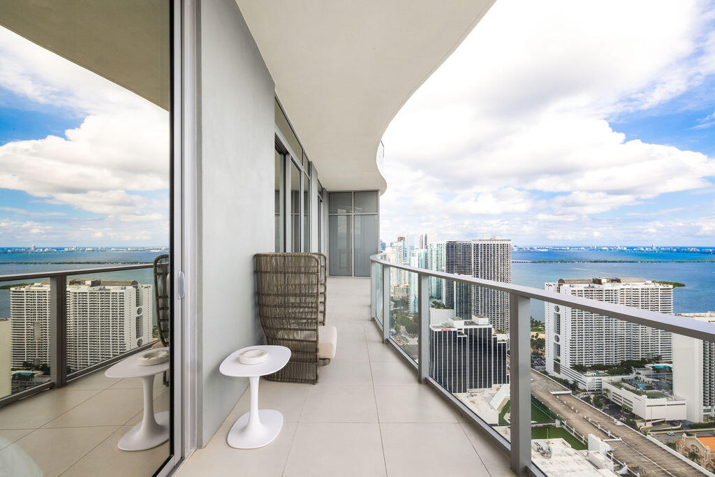 Expansive wrap-around balcony featuring large-format tile flooring, a curved architectural design, and floor-to-ceiling glass paneling with metal railing