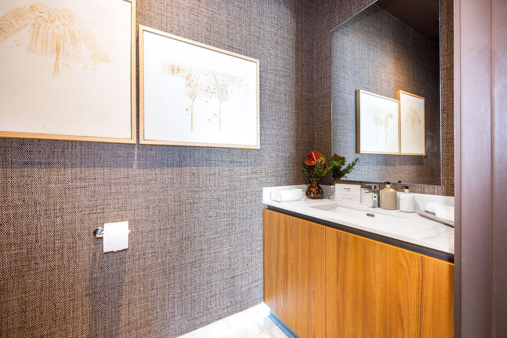 Textured wall covering, wood-finish vanity cabinet, light-toned countertop with an integrated rectangular sink, wall-mounted mirror, and chrome-finish fixtures