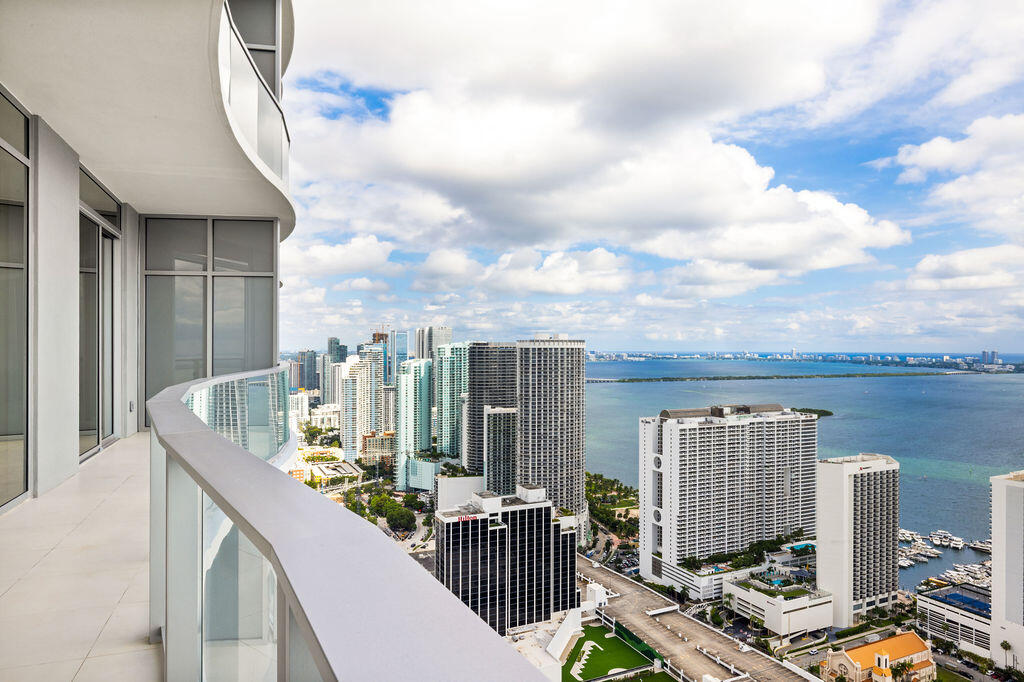 Curved exterior balcony with glass railing, large-format tile flooring, and expansive floor-to-ceiling windows