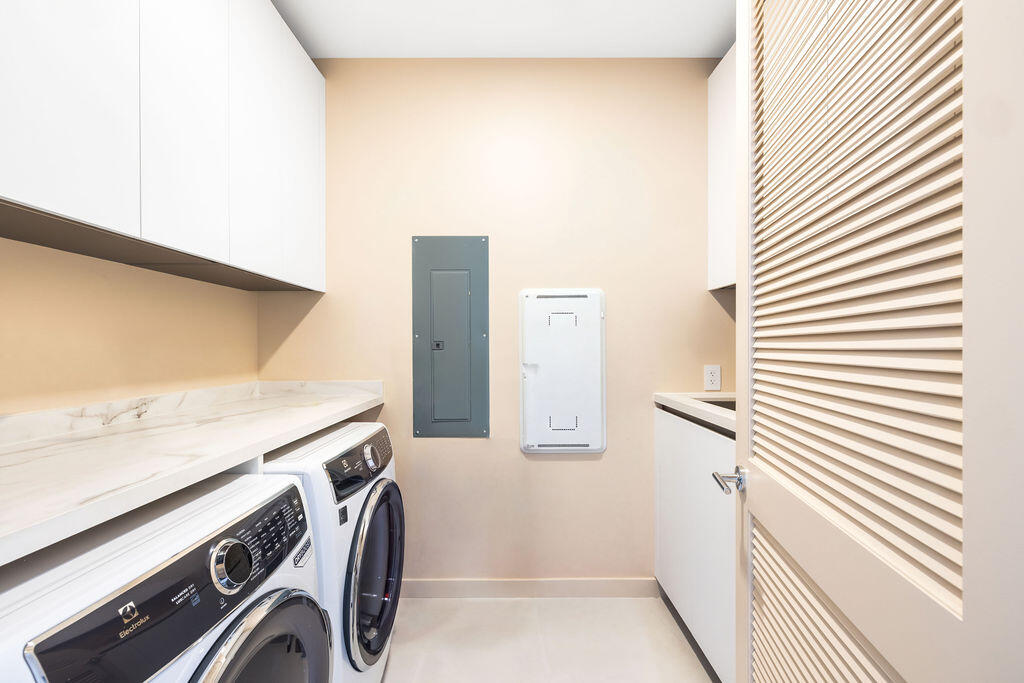 Laundry room featuring white shaker-style wall cabinetry, stone-finish countertops, and a louvered door