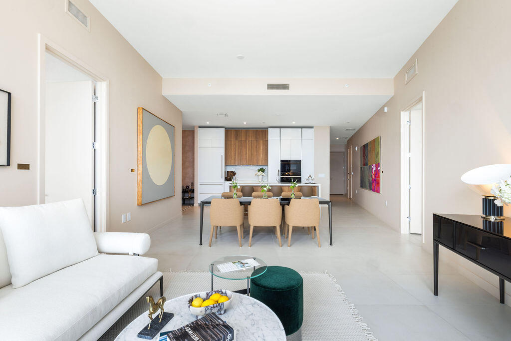 Open-concept interior featuring light-toned flooring, high ceilings, custom wood and white cabinetry, a built-in oven, and a kitchen island with stone countertop