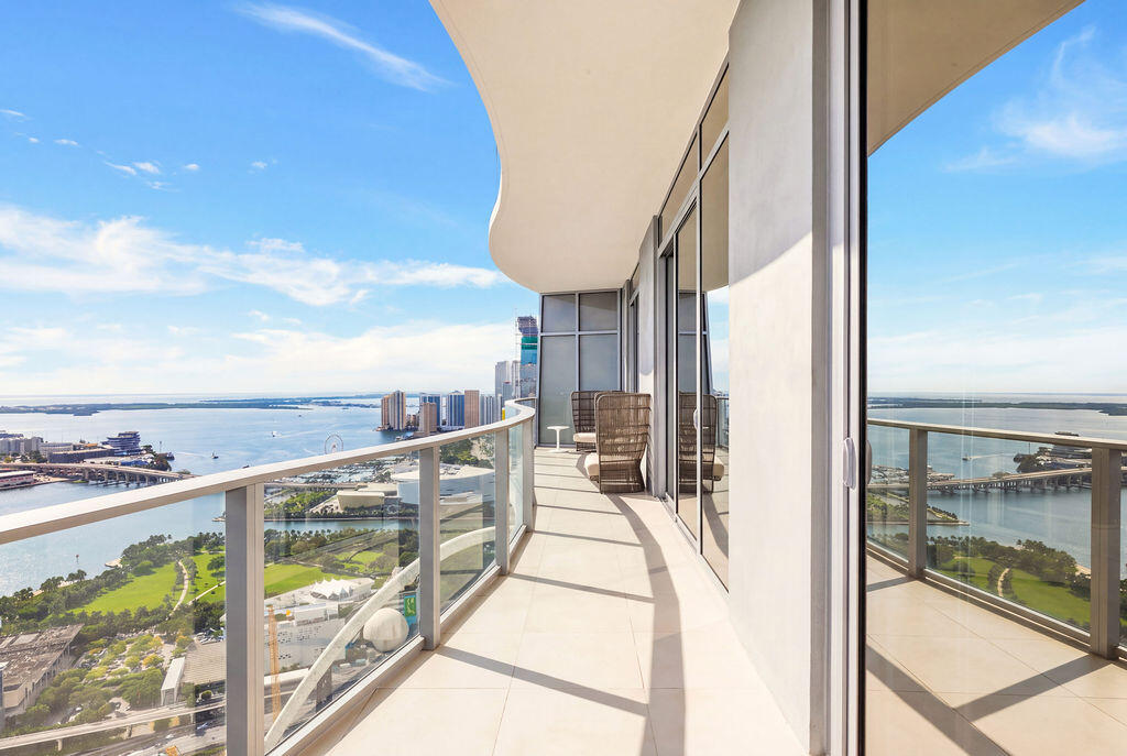 Expansive covered balcony featuring glass railings, large-format tile flooring, and floor-to-ceiling glass doors
