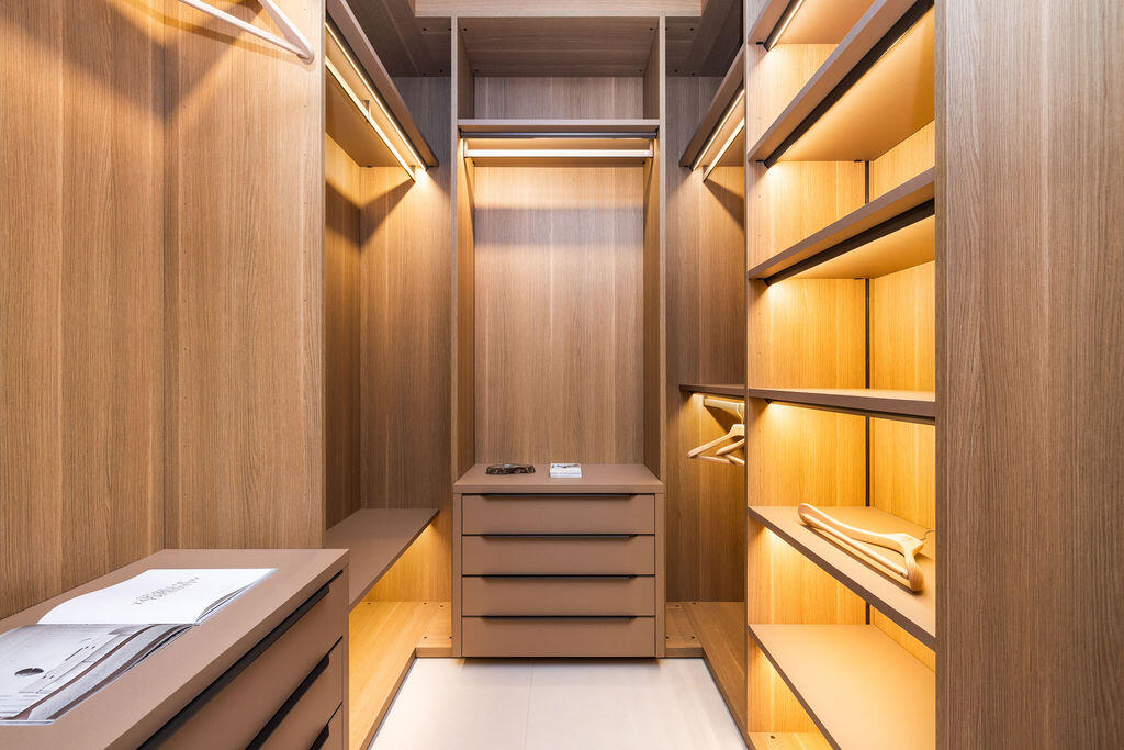 Custom walk-in closet featuring floor-to-ceiling wood-finish cabinetry, integrated linear task lighting, built-in drawer units, and open shelving