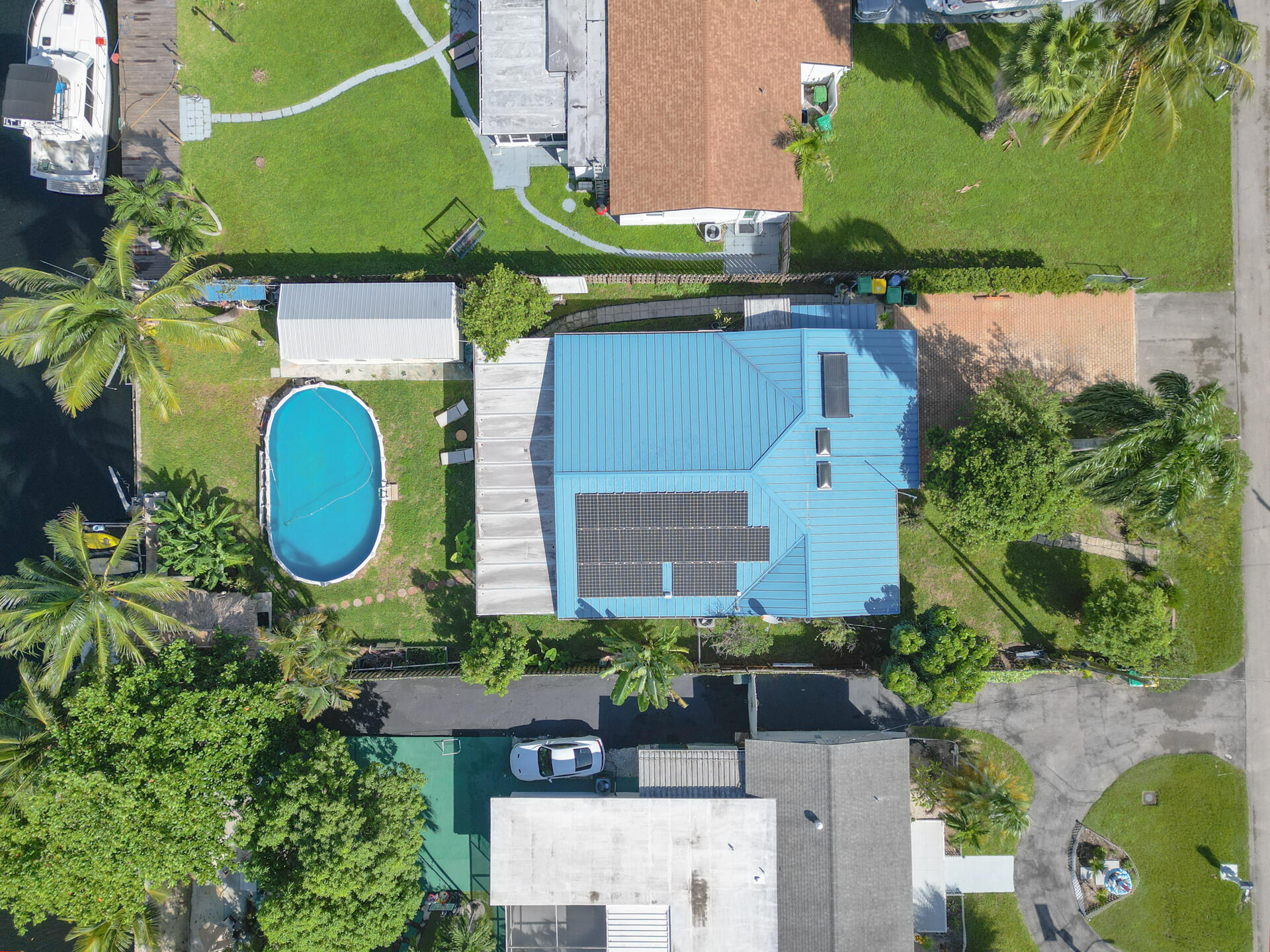 Aerial view of the property featuring a metal roof with 28 integrated solar panels, an inground pool, a wooden deck, and direct water frontage with private dockage