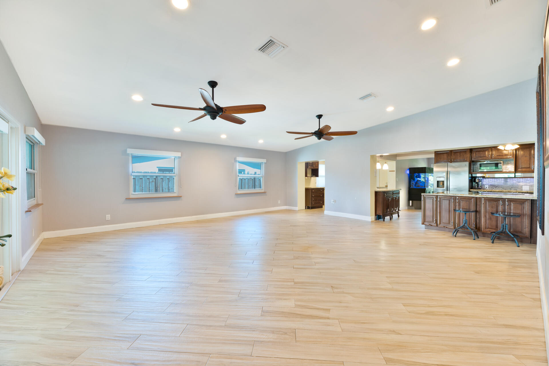 Open-concept interior featuring light-toned ceramic plank flooring, recessed lighting, dual ceiling fans, and a kitchen with stained wood cabinetry and a breakfast bar