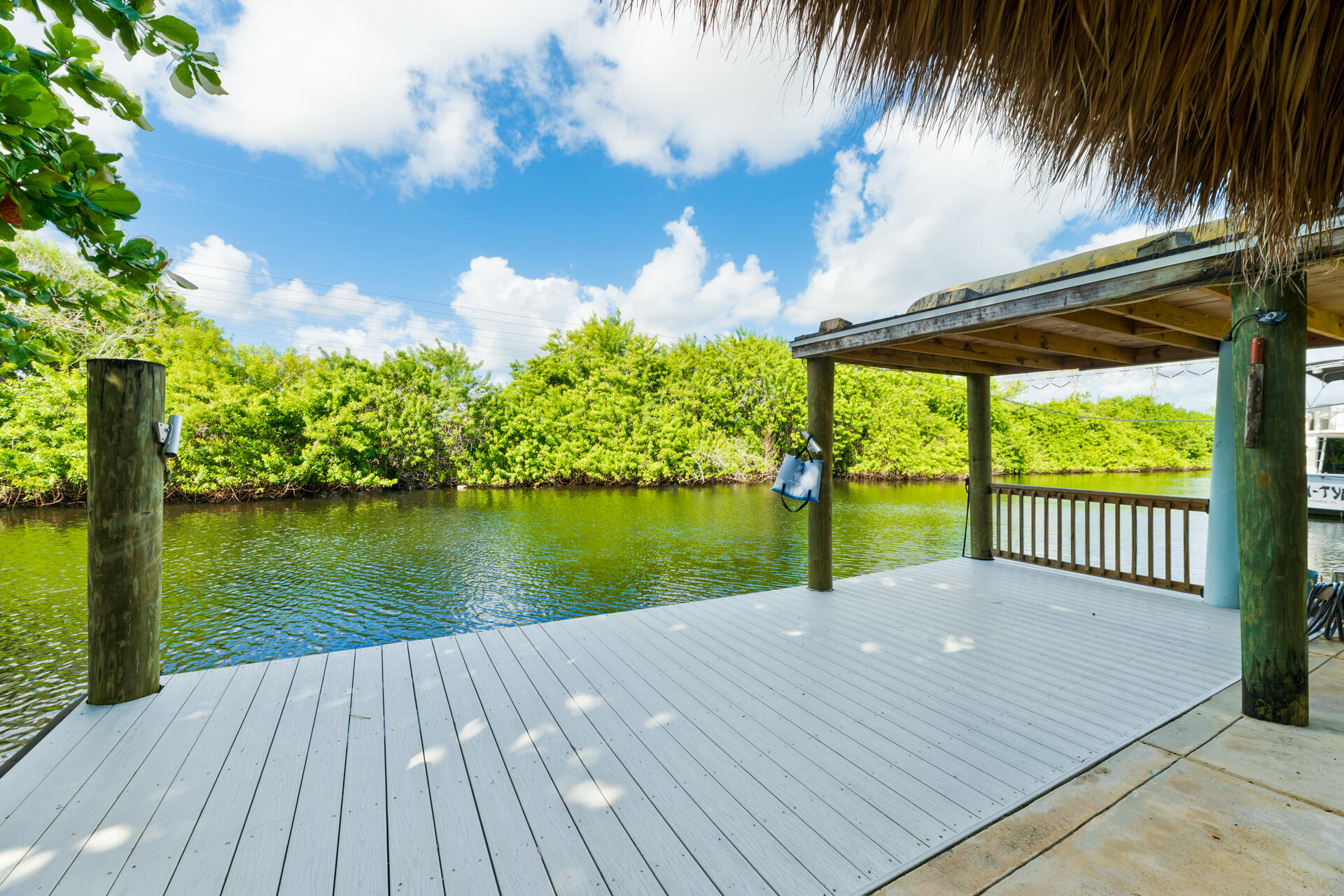 Waterfront dock featuring composite decking, a roof structure, timber pilings, and a wooden railing
