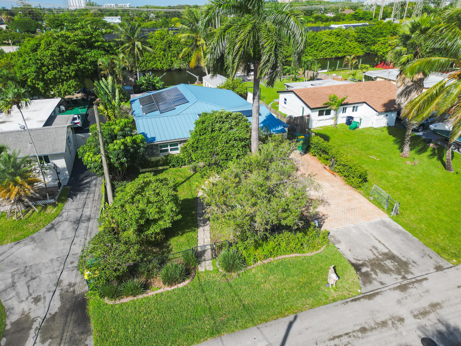 Metal roofing system featuring 28 mounted solar panels, paved driveway, stone-accented exterior, and manicured landscaping with mature palm trees