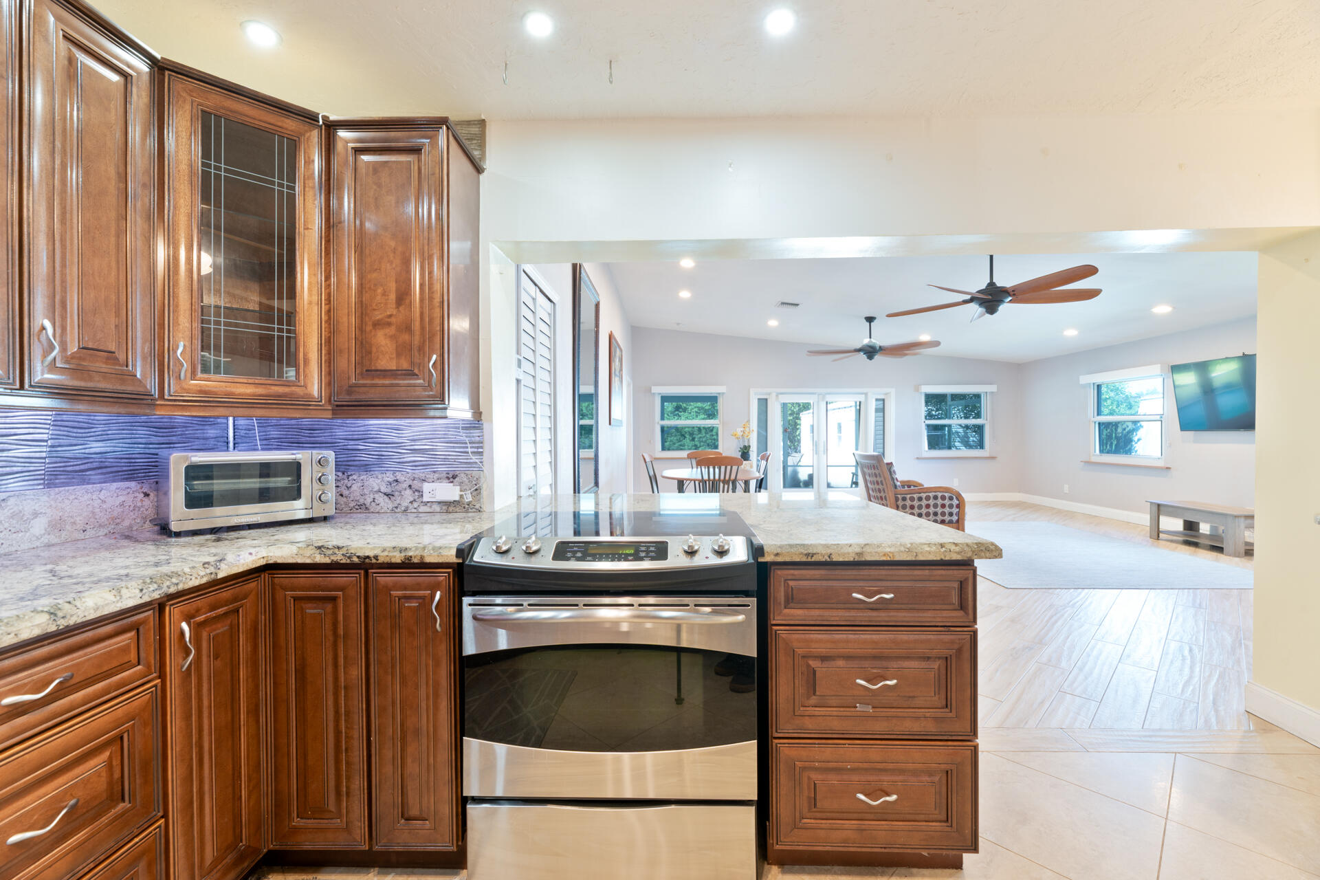 Kitchen featuring stained wood cabinetry, stone countertops, a tiled backsplash, built-in stainless steel appliances, and tile flooring