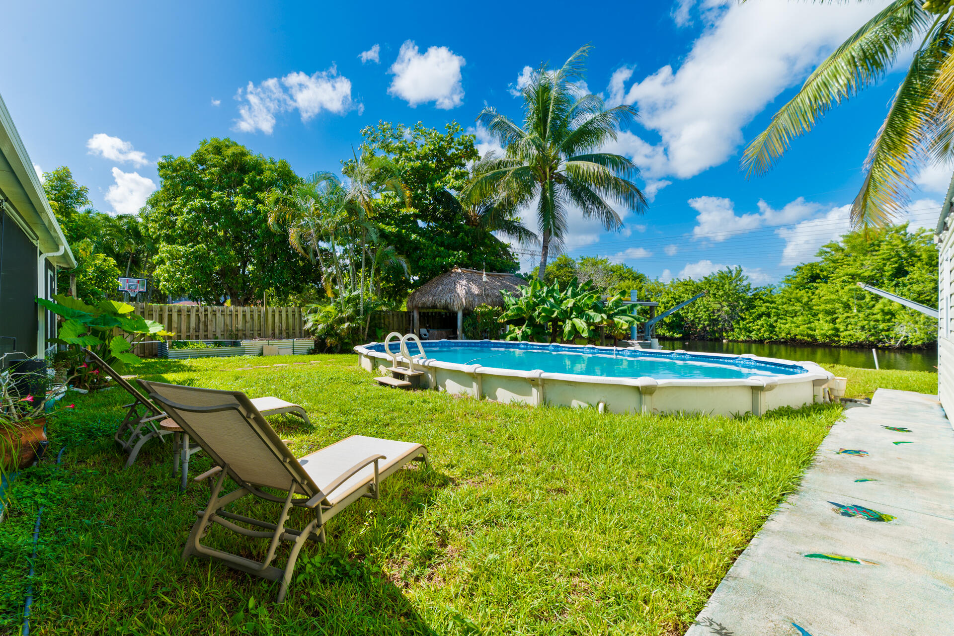 Backyard featuring an above-ground pool, grass lawn, thatch-roofed cabana, and water frontage