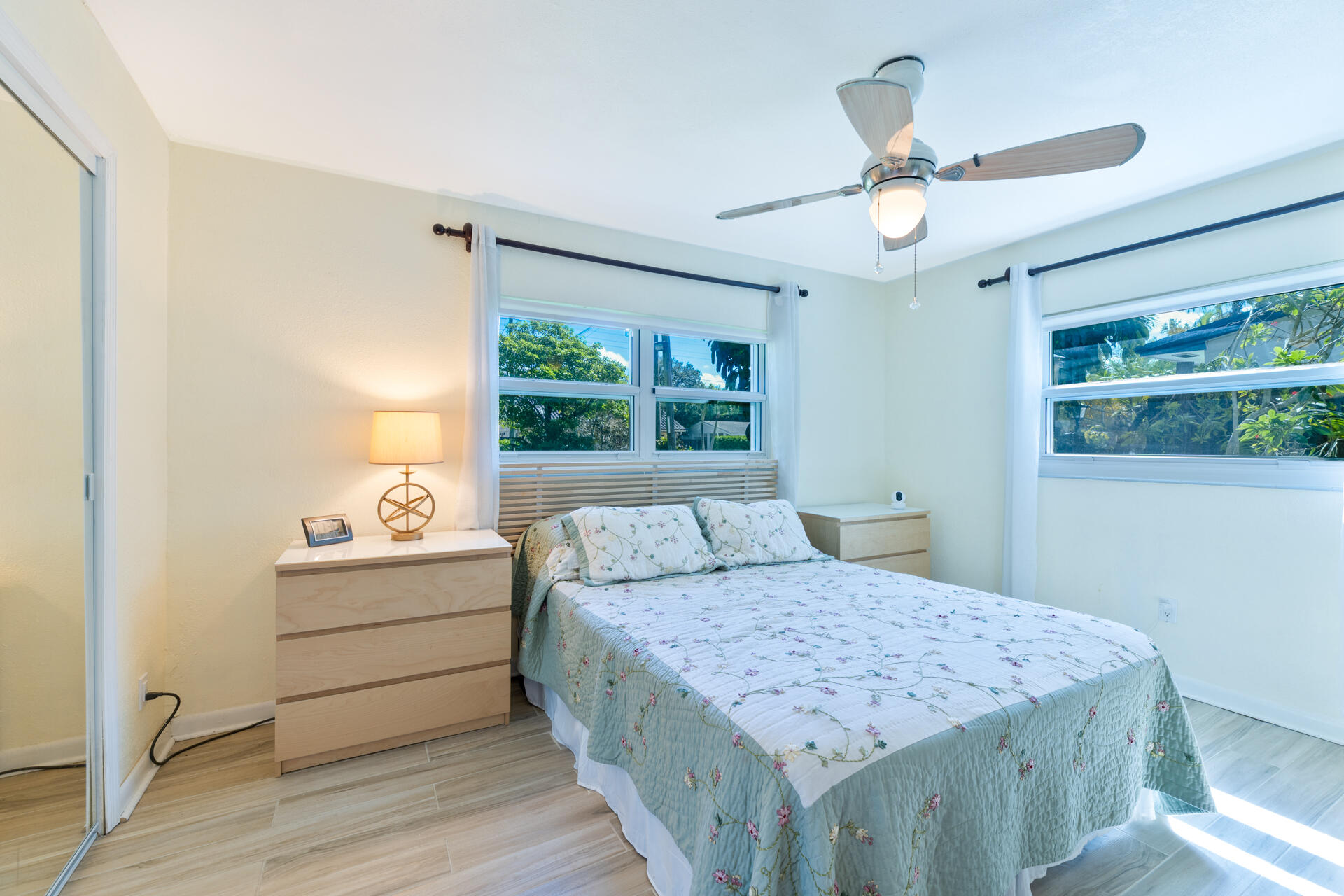 Neutral-toned room featuring ceramic plank flooring, a ceiling fan with integrated lighting, dual windows, and a mirrored sliding closet door
