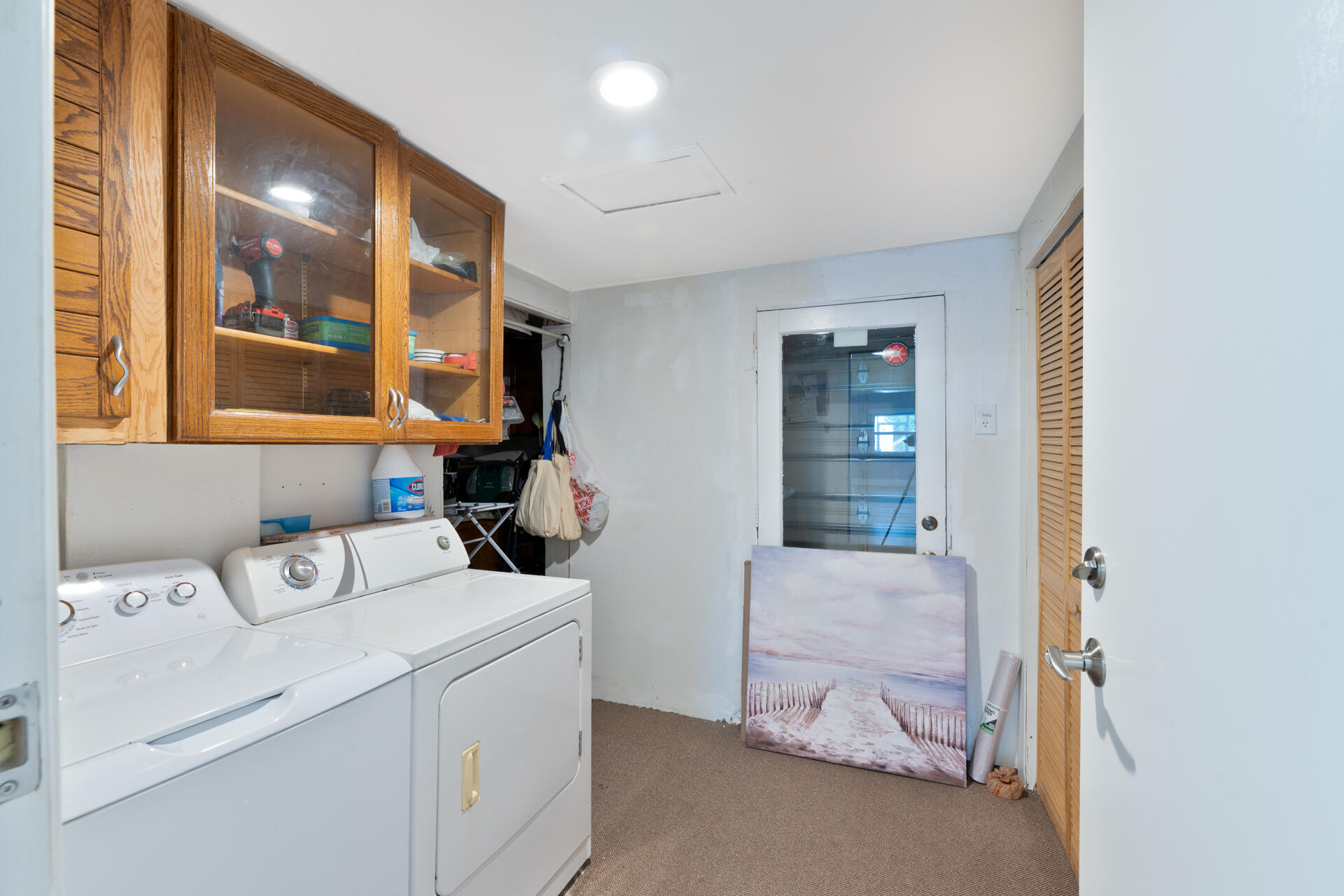 Utility area featuring wall-mounted wood cabinetry with glass-panel doors, louvered closet doors, and an exterior door with integrated window