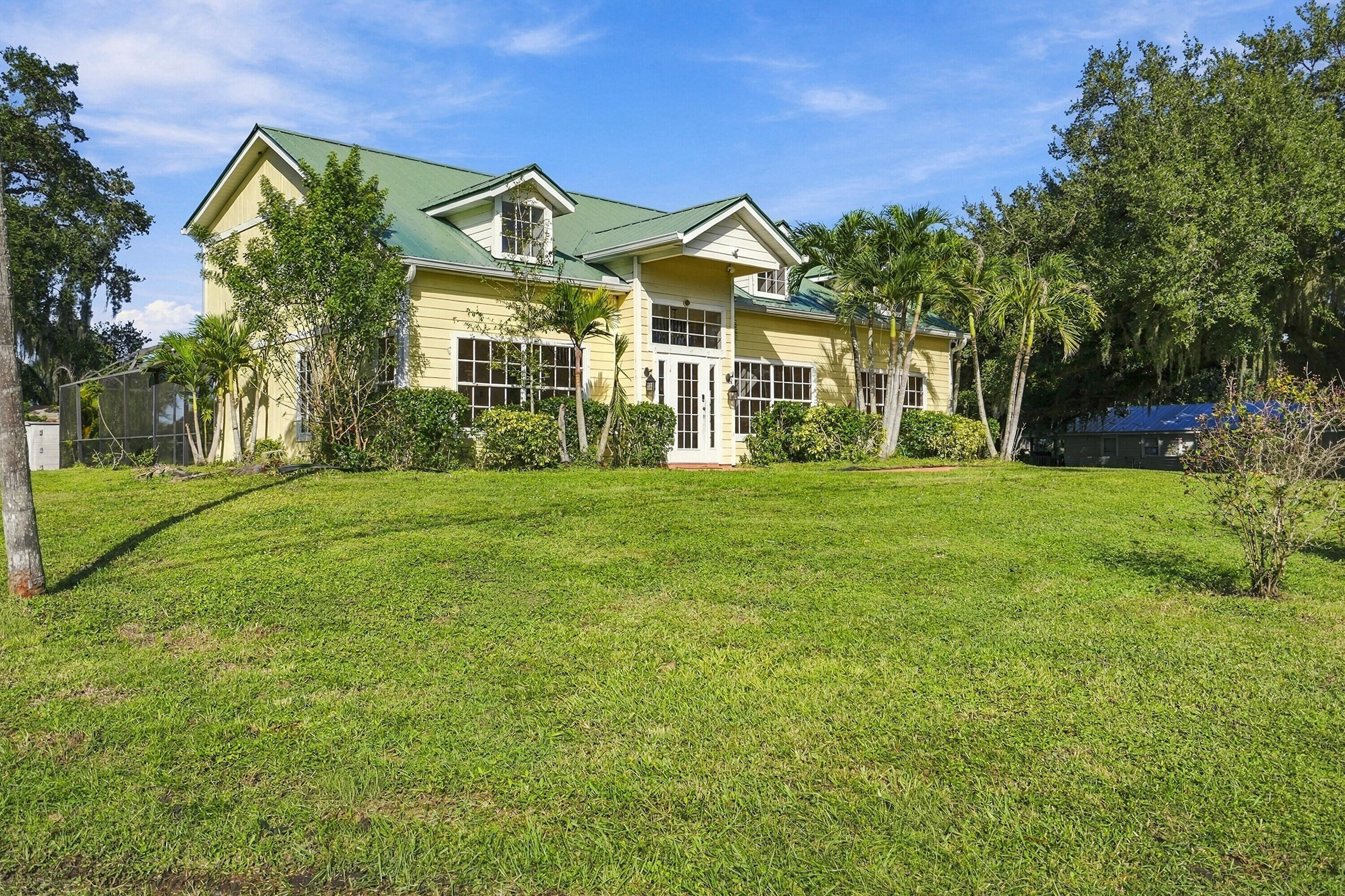 Two-story home with a green metal roof, light yellow horizontal siding, multi-pane windows, and a screened-in enclosure Two-story home with a green metal roof, light yellow horizontal siding, multi-pane windows, and a screened-in enclosure