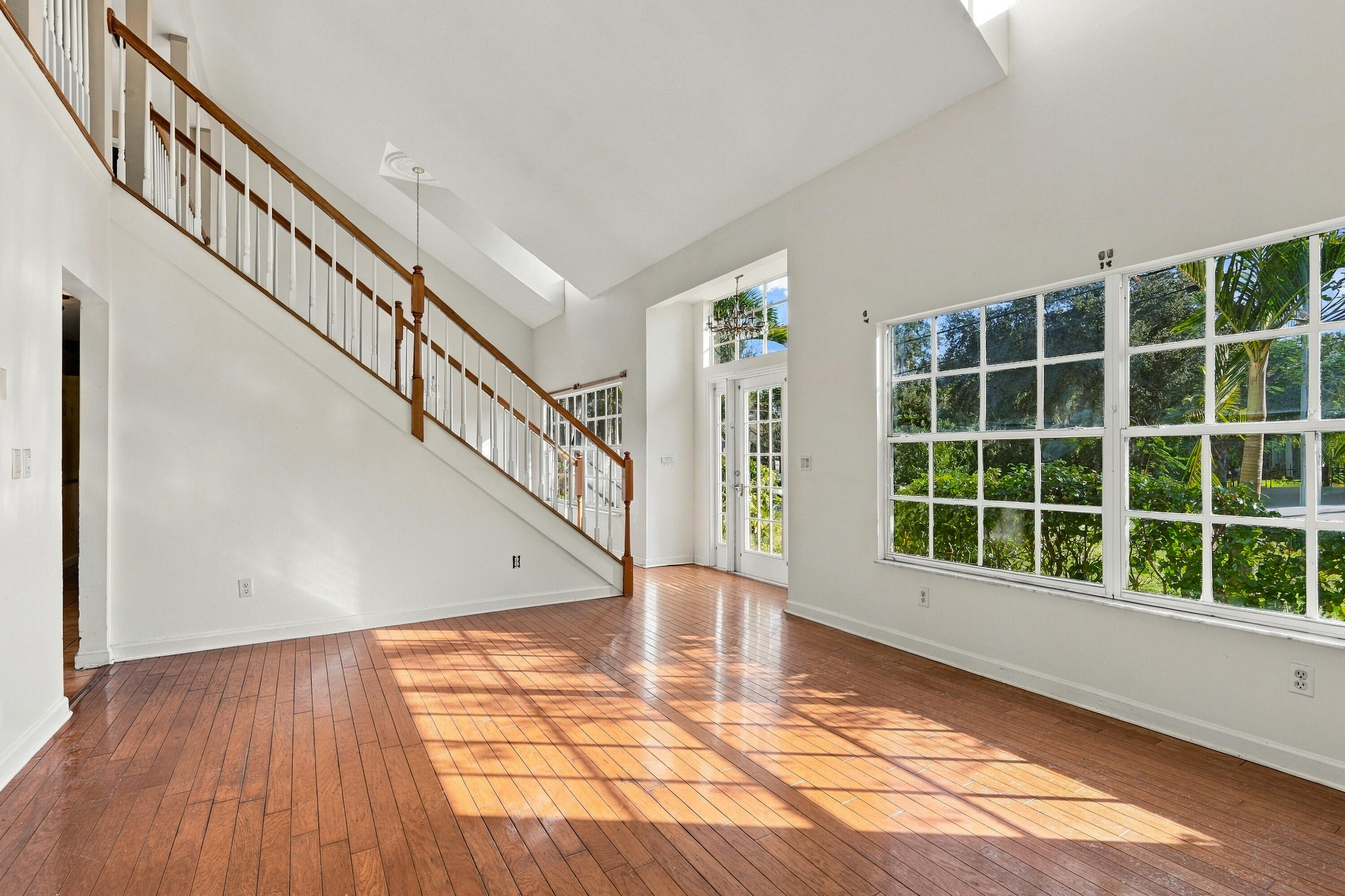 Vaulted ceilings, wood-finish flooring, staircase with wood railings, multiple pane windows, and a glass-paneled entry door