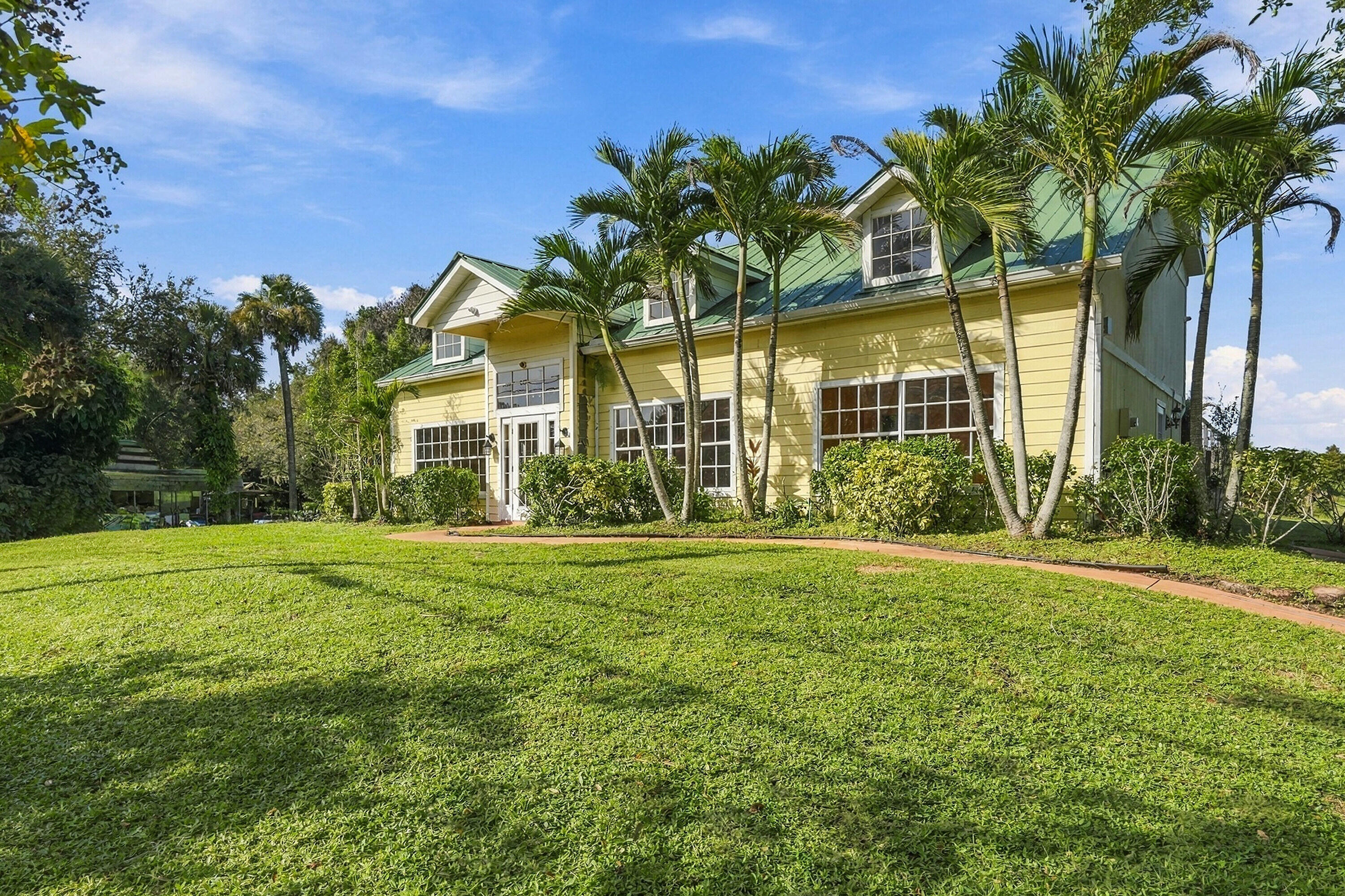 Exterior featuring yellow horizontal lap siding, a pitched green metal roof, multiple dormer windows, large multi-pane windows, and a paved walkway Exterior featuring yellow horizontal lap siding, a pitched green metal roof, multiple dormer windows, large multi-pane windows, and a paved walkway