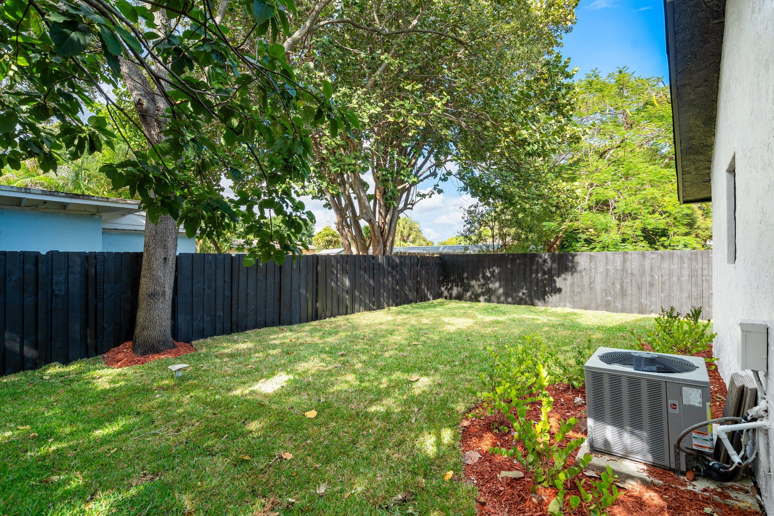 Backyard featuring a manicured lawn, perimeter wood fencing, established trees, and organic mulch landscaping