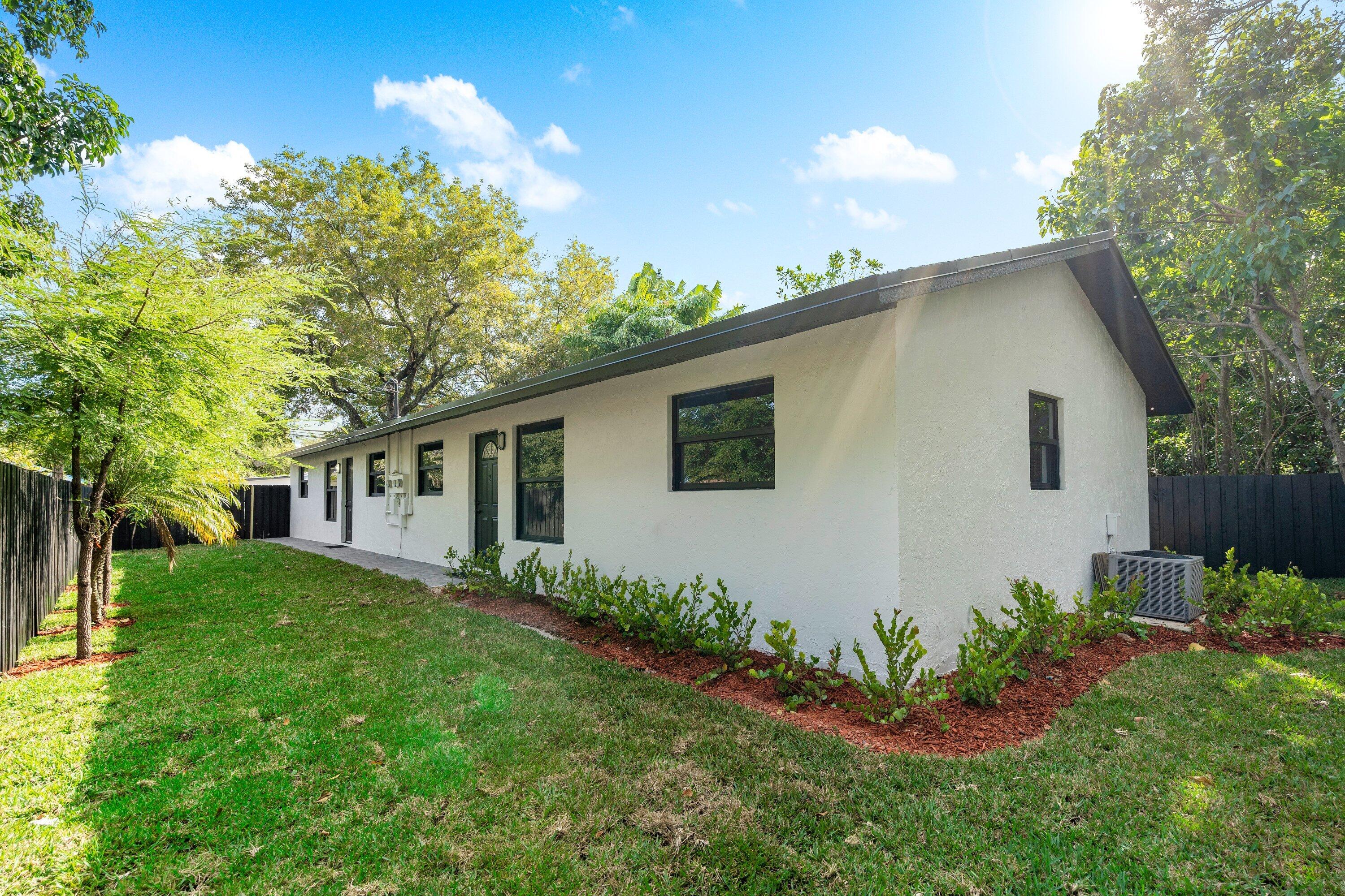 Stucco exterior featuring dark-trimmed windows, a multi-paneled door, manicured landscaping with mulch beds, and an enclosed fenced yard