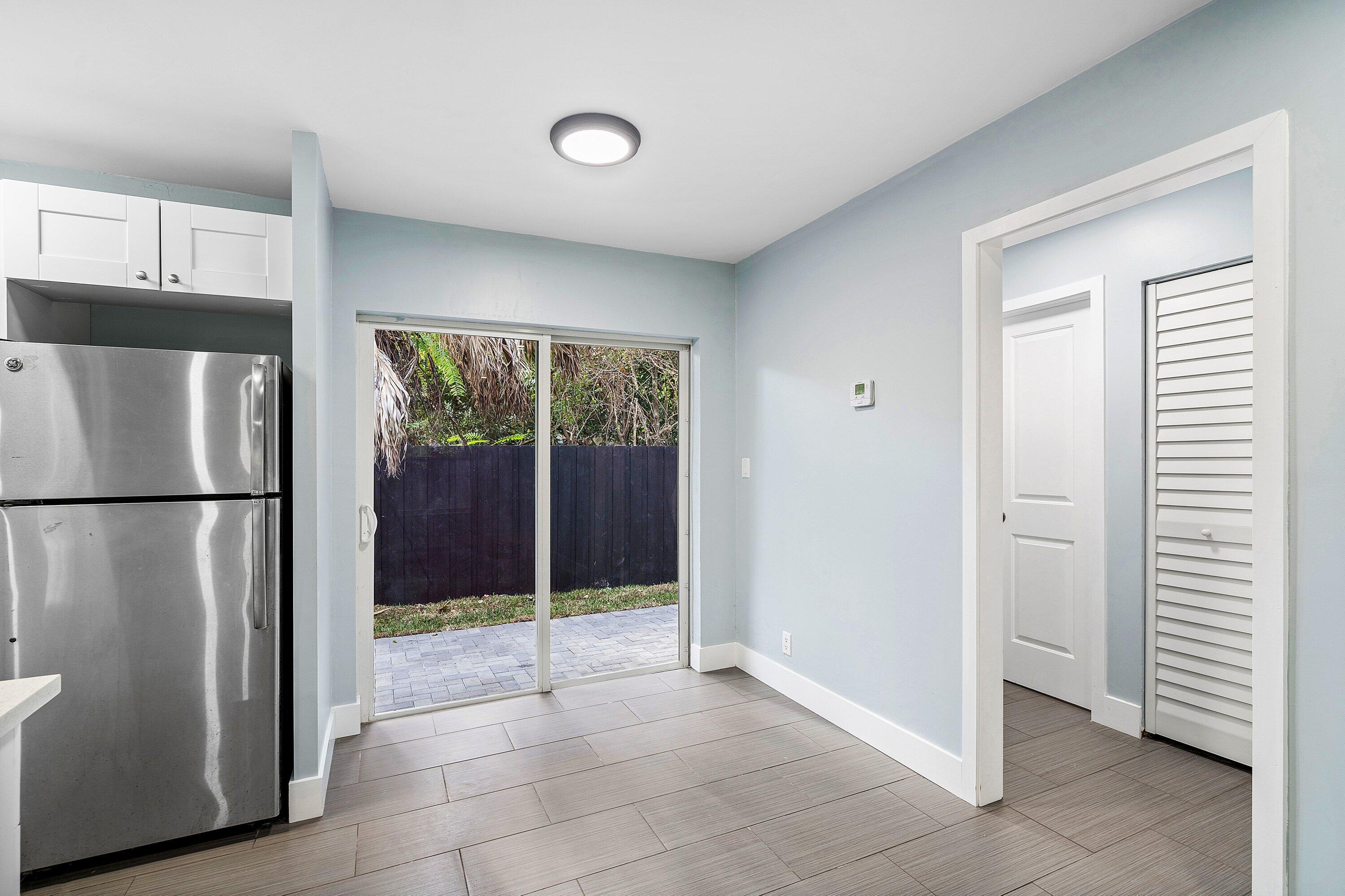 Kitchen space featuring white shaker-style cabinetry, stainless steel refrigerator, tile flooring, and sliding glass doors leading to a paved patio