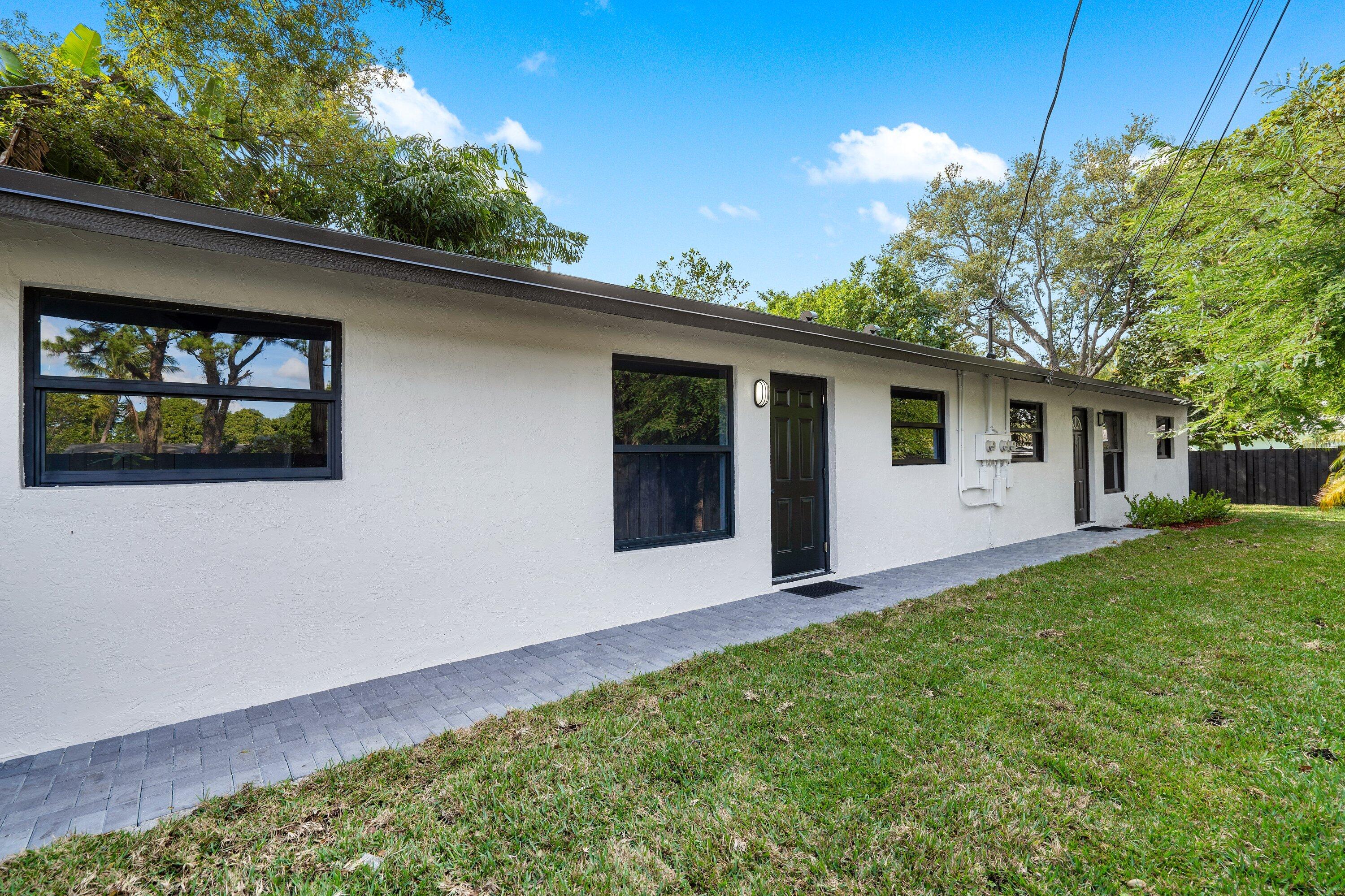 Stucco exterior featuring dark-framed windows, a paver walkway, and a manicured lawn