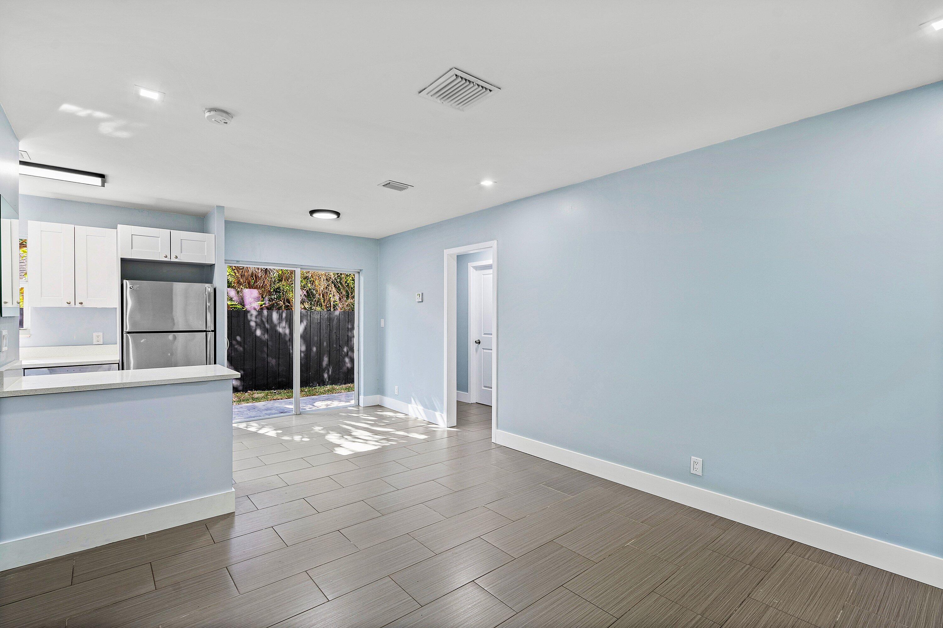 Open-concept space featuring ceramic tile flooring, kitchen with white cabinetry, stainless steel refrigerator, and glass sliding doors