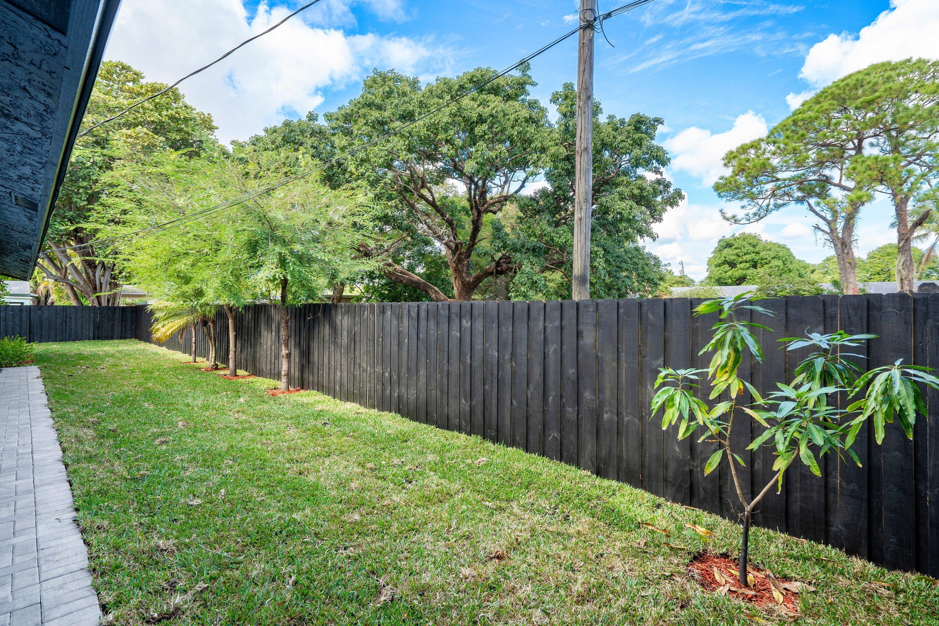 Private backyard featuring a paved stone walkway, perimeter dark-stained vertical wood fencing, manicured lawn, and mature canopy trees