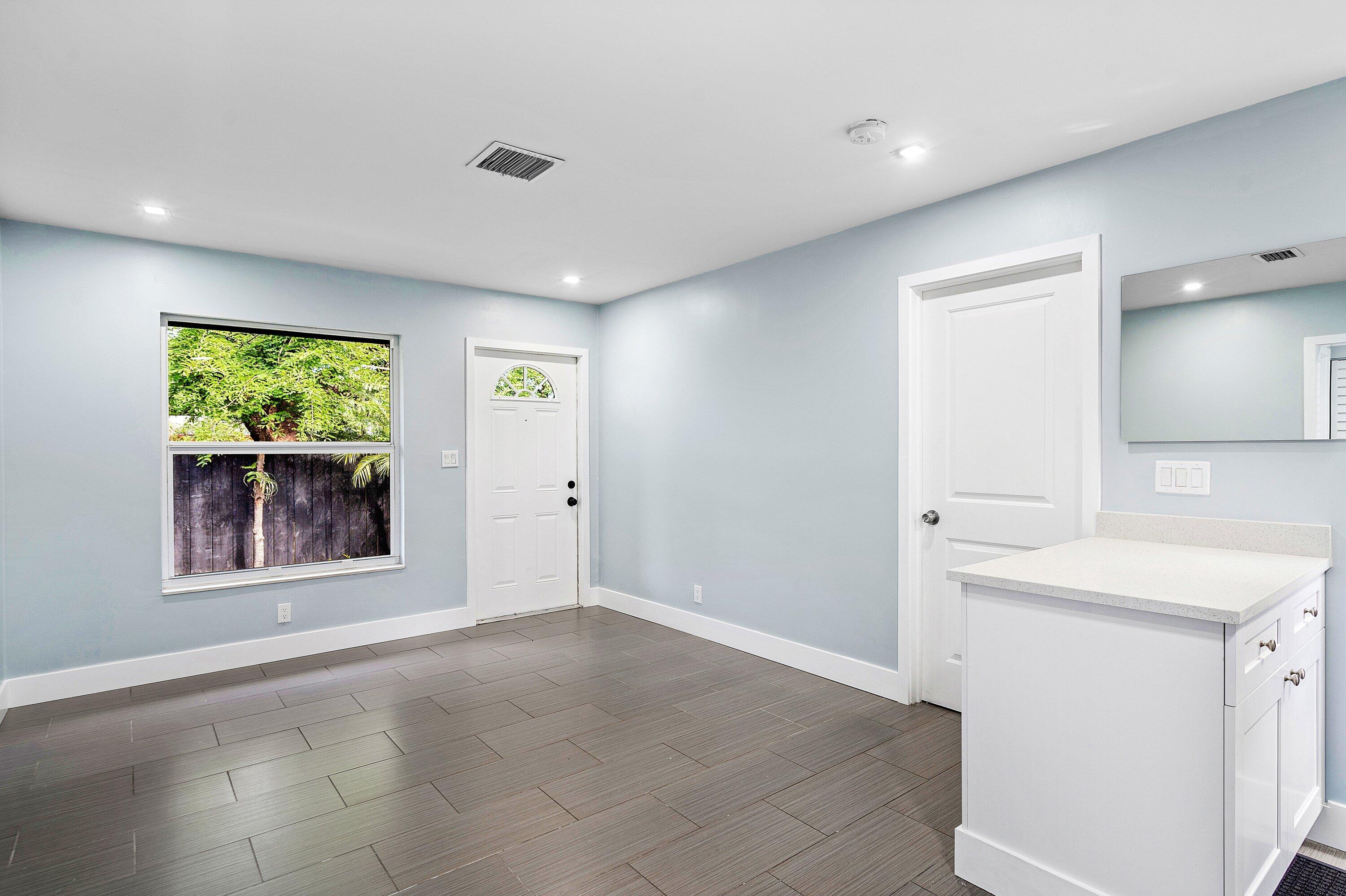 Neutral-toned interior featuring large-format rectangular floor tile, recessed lighting, white built-in cabinetry with a stone-surface countertop, and a single-hung window