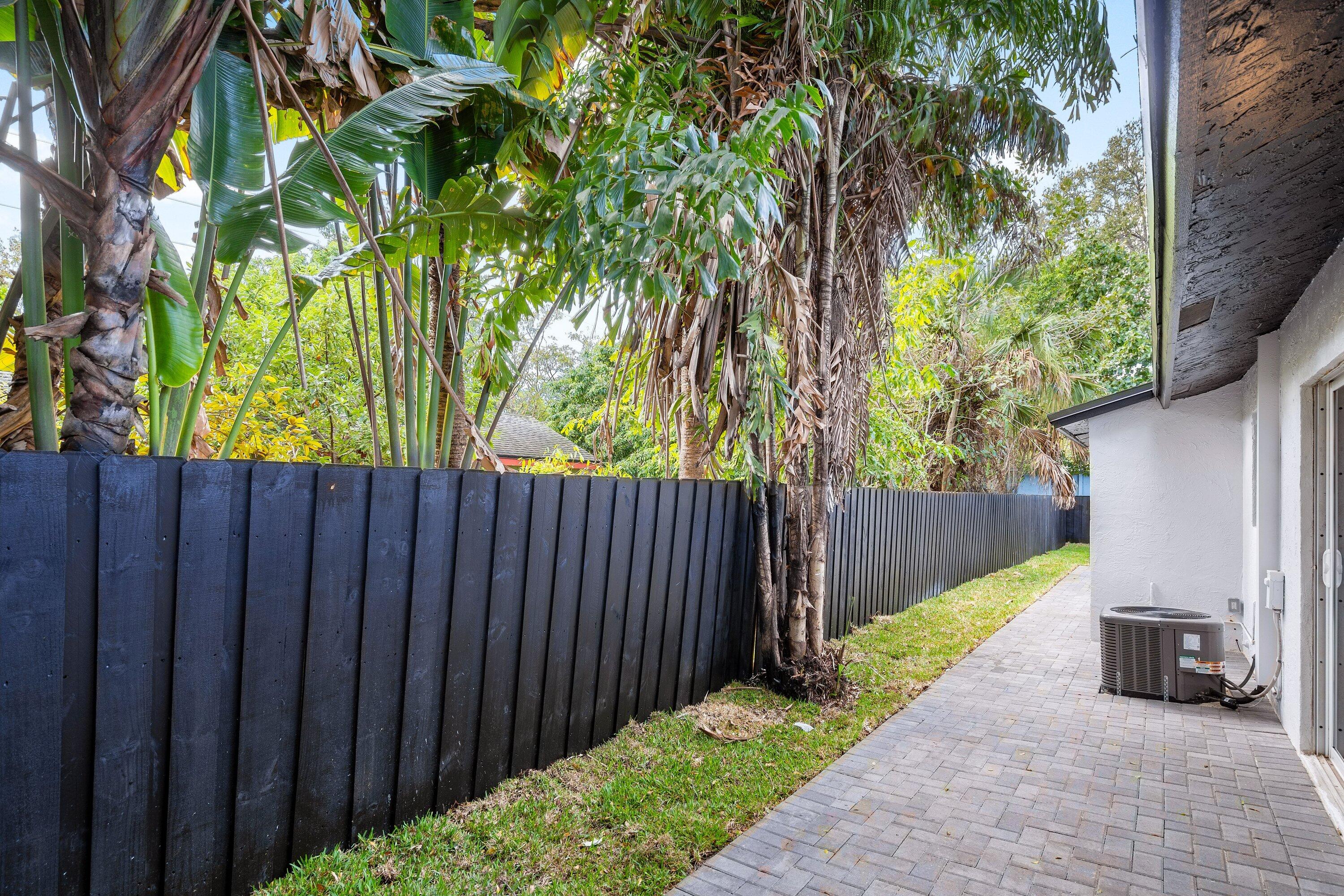 Side yard featuring a paver stone patio, a dark wood-finish privacy fence, and mature palm trees