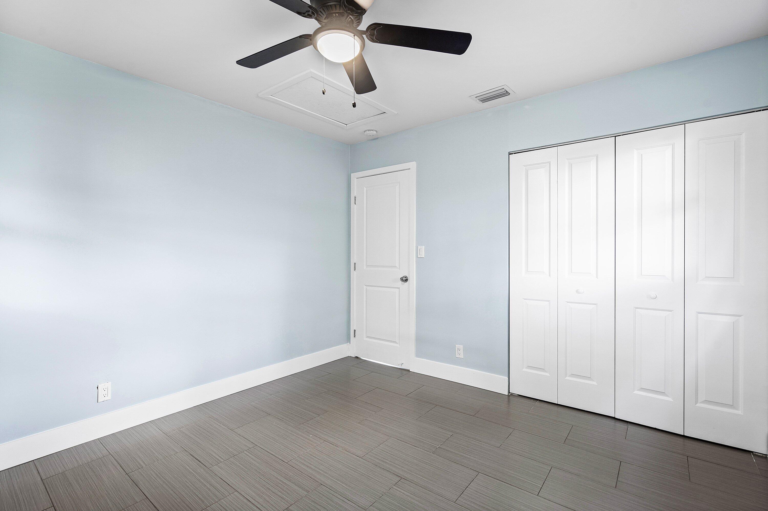 Room featuring large-format tile flooring, a multi-panel door, built-in closet with folding doors, and a ceiling-mounted light fixture with fan