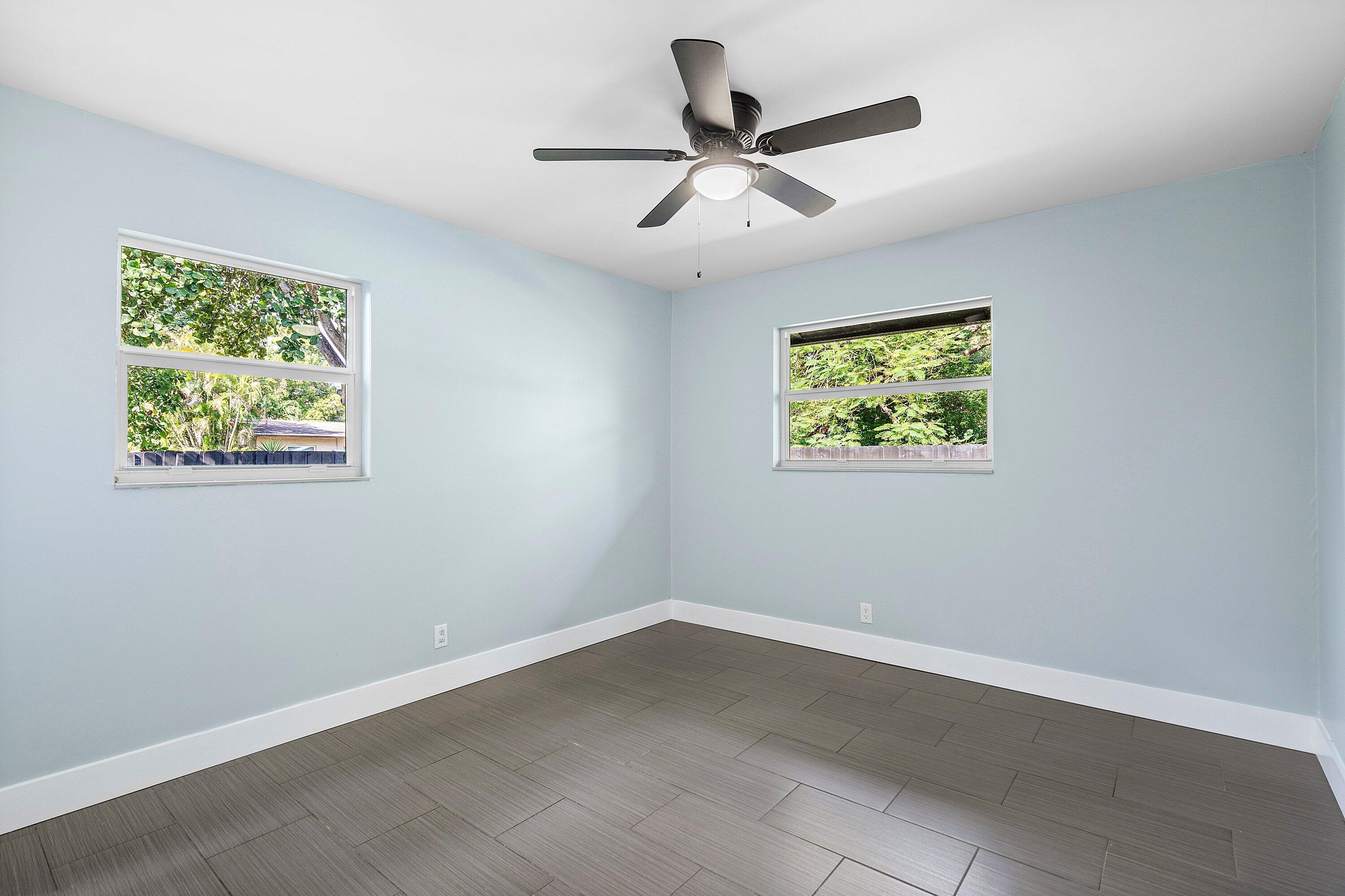 Interior space featuring neutral wall paint, dark tile flooring, dual windows, and a central ceiling fan with integrated lighting