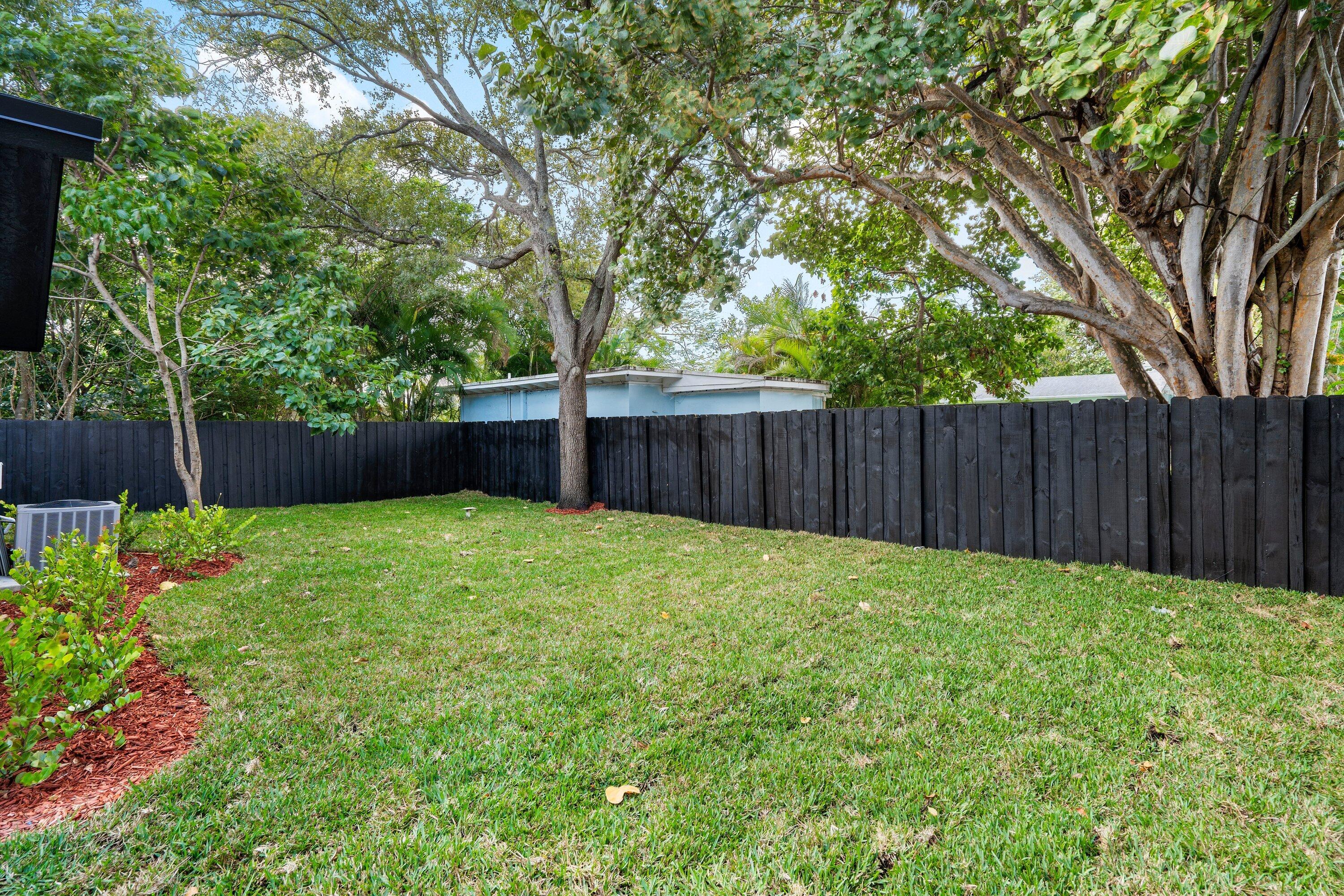Private backyard featuring a manicured lawn, wood-finish privacy fencing, and mature trees