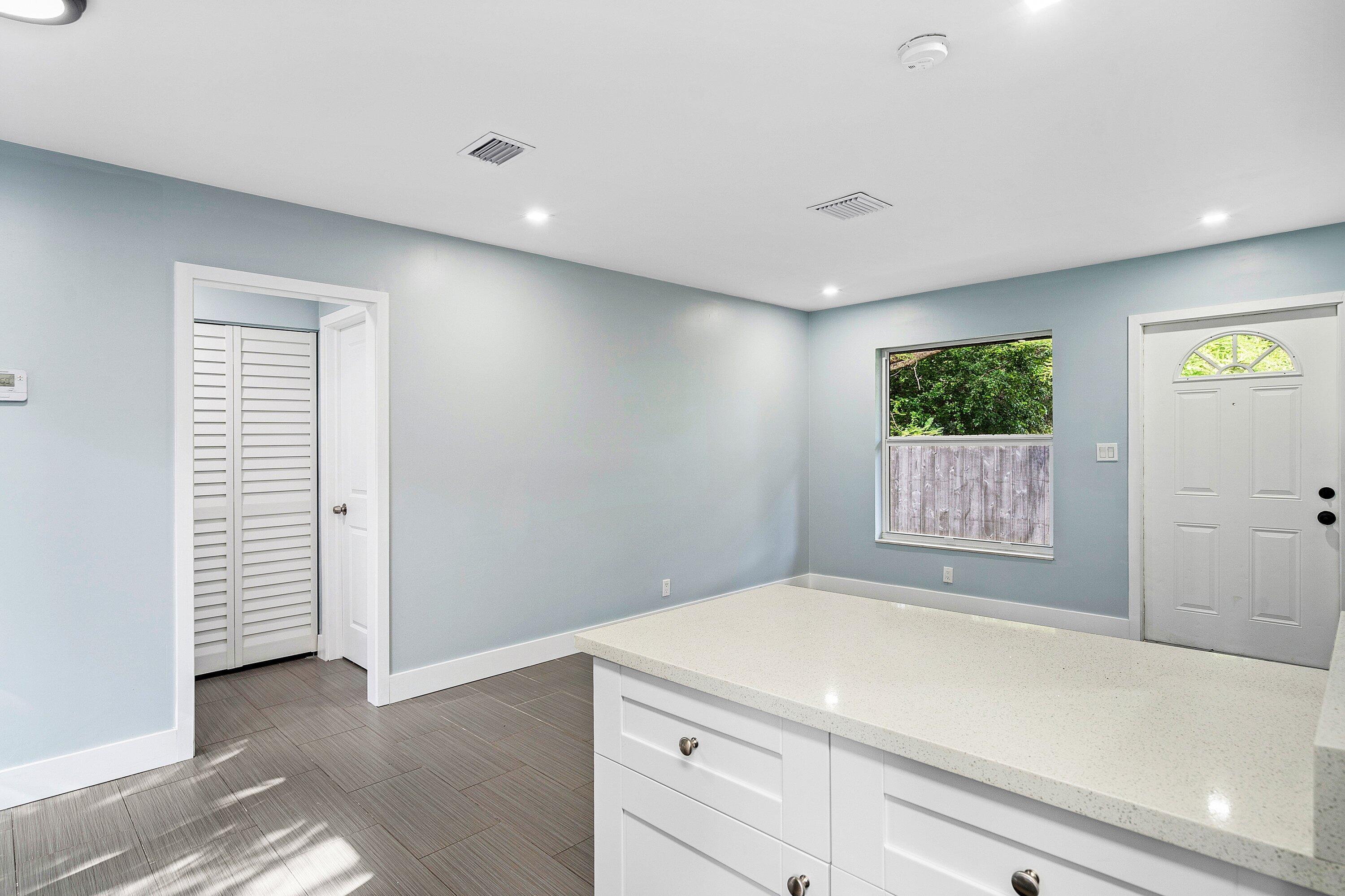 Interior featuring white built-in cabinetry with stone-finish countertops, grey tile flooring, louvered closet doors, and a paneled exterior door with glass insert